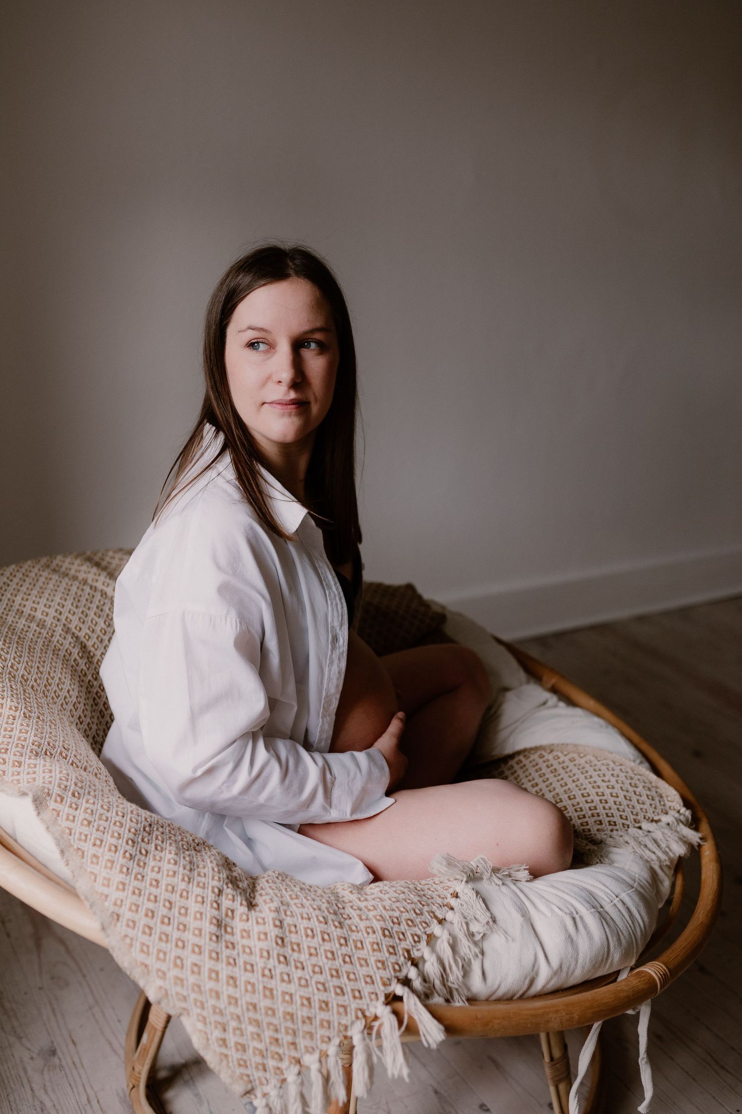Person in white shirt sitting in a cozy round wicker papasan chair with textured throw blanket on hardwood floor.