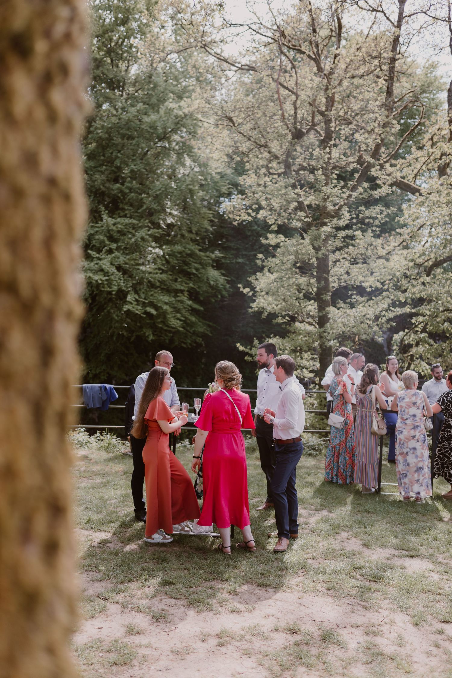A group of guests mingle outdoors at a garden party on a sunny day surrounded by blooming trees.