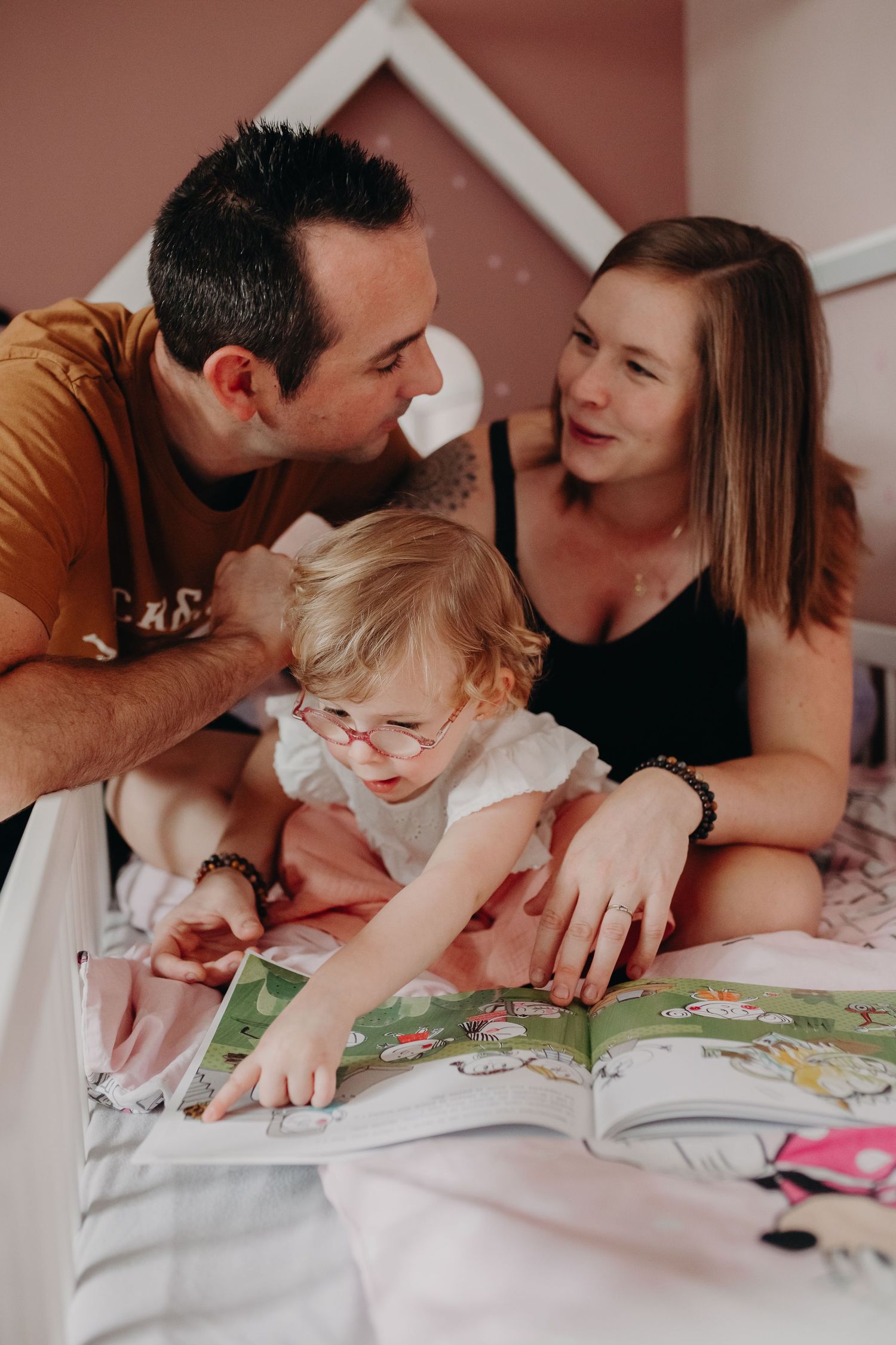 Family shares a joyful moment while reading a picture book together at home on white bedding.