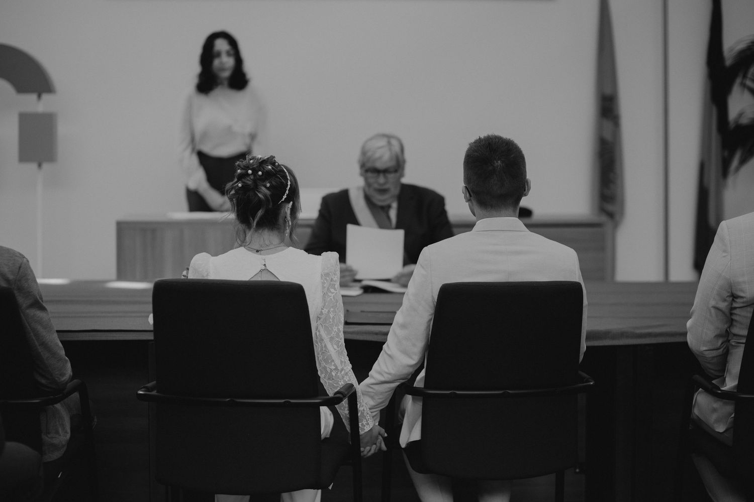 Two people sitting in chairs before an officiant during a wedding ceremony in black and white.