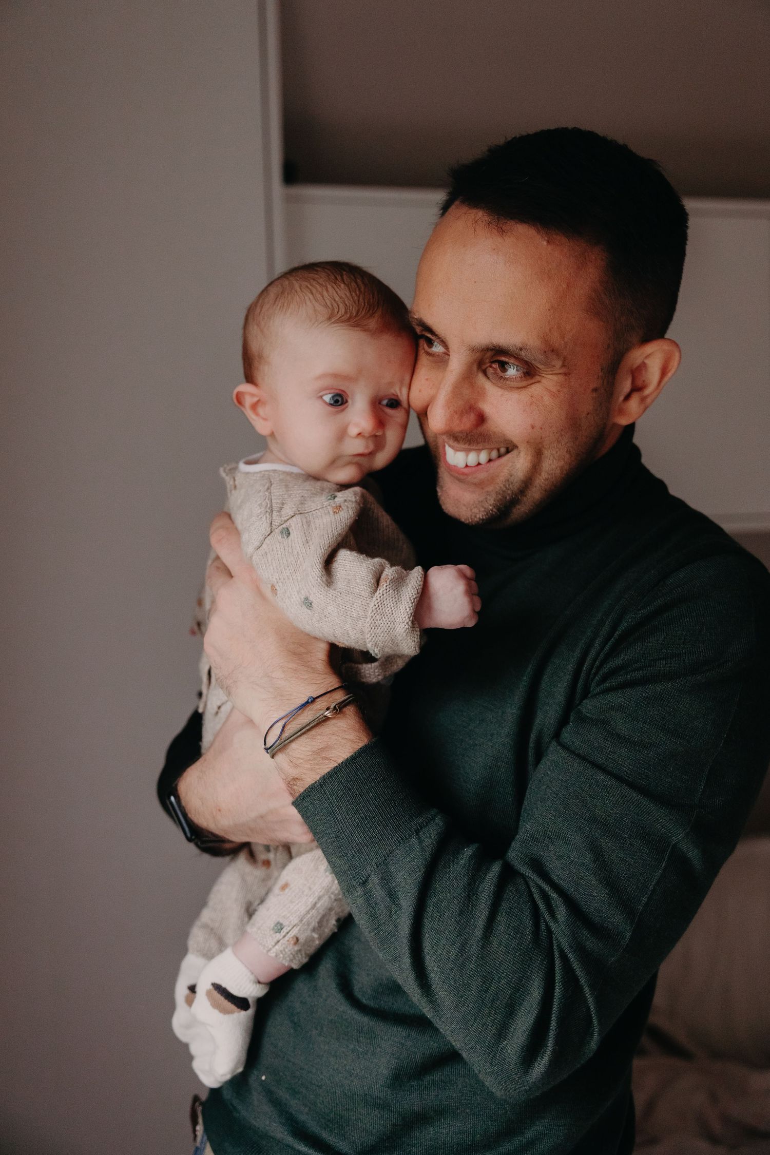 A parent in a dark sweater holds and lovingly embraces a small baby wearing light colored clothing.