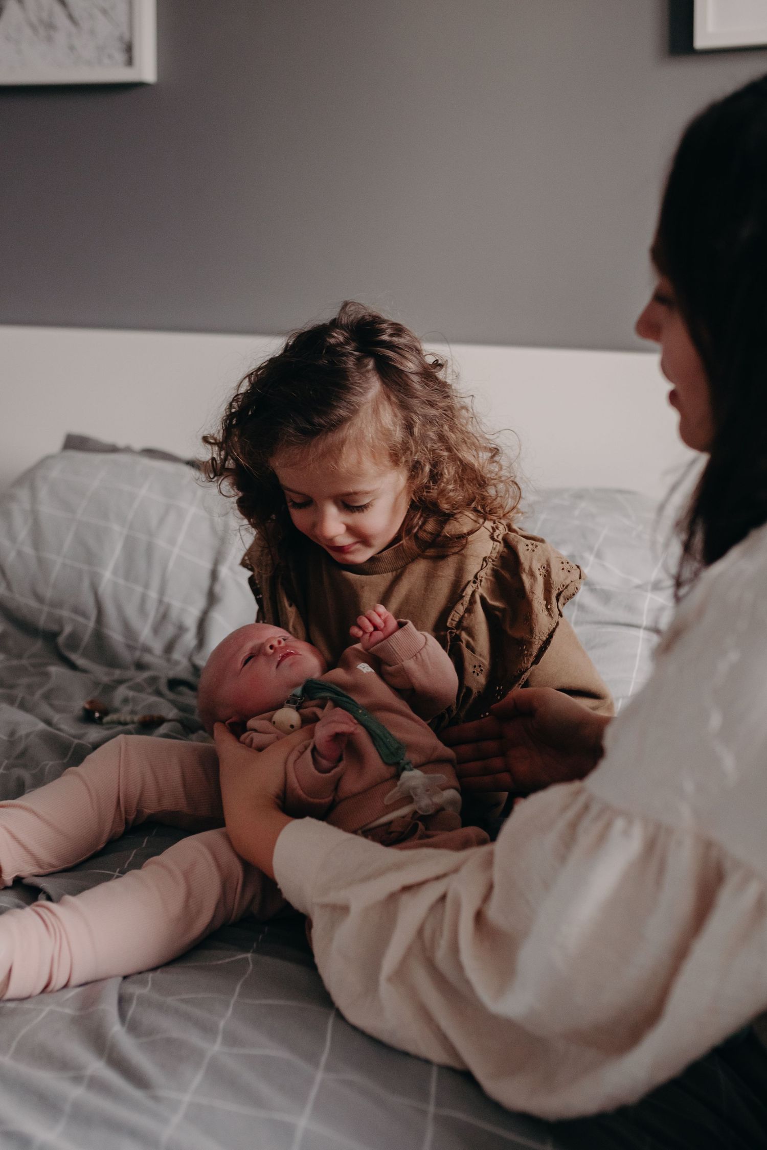 A series of intimate black and white photos showing tender moments between a young child and an infant on a bed.