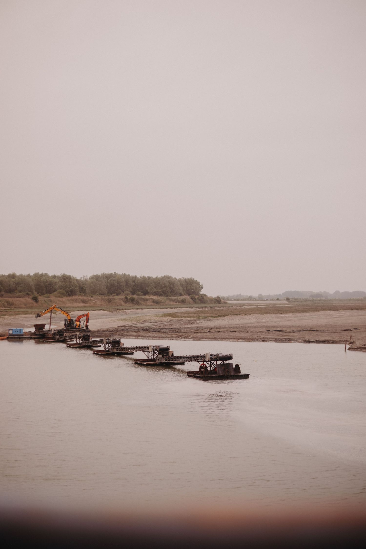 Several wooden boats moored in a line along a misty riverbank with barren landscape in the background.