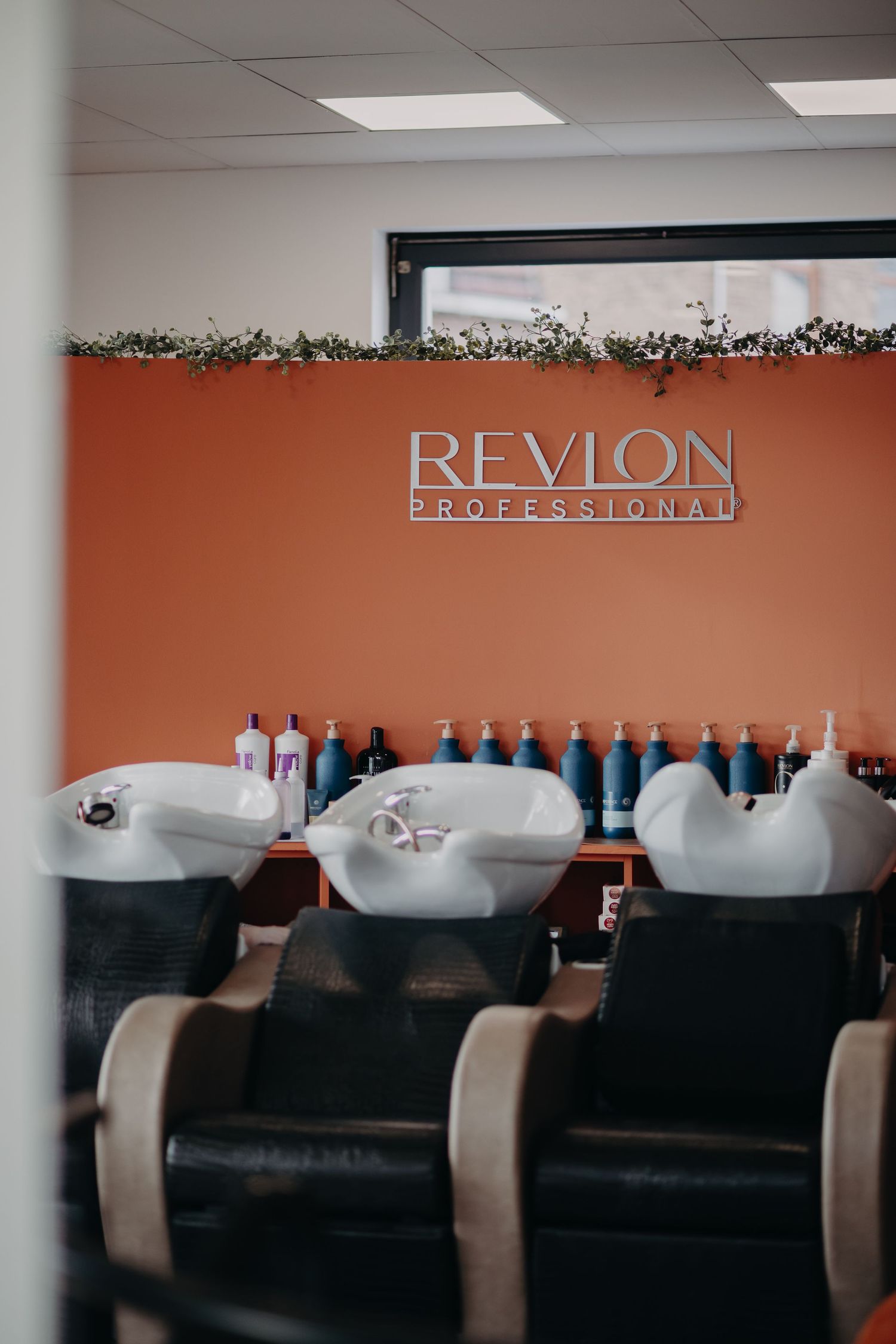 Hair washing station with Revlon Professional signage and products at a modern salon interior.