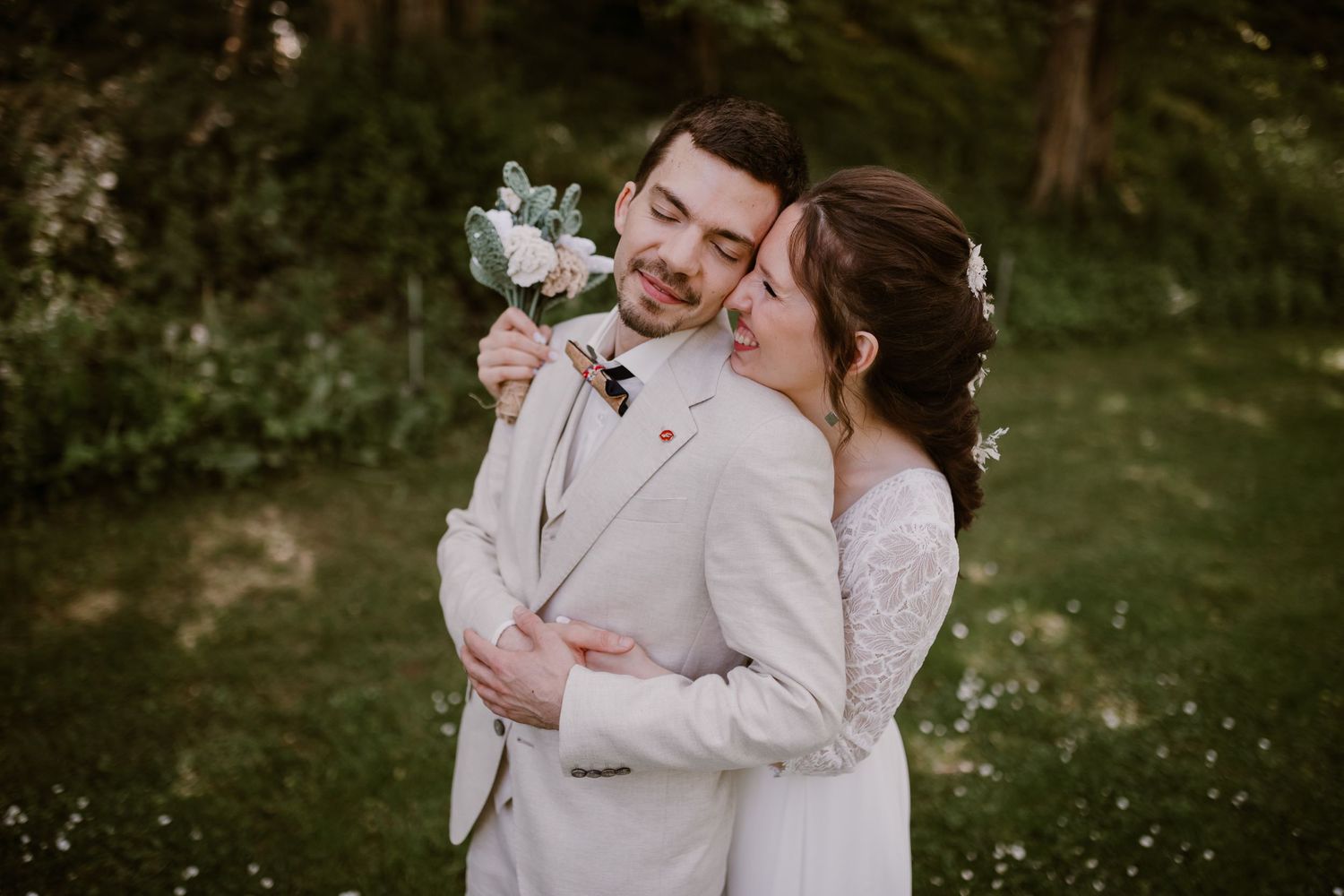 A couple shares an intimate moment outdoors in soft white wedding attire with floral bouquet details.