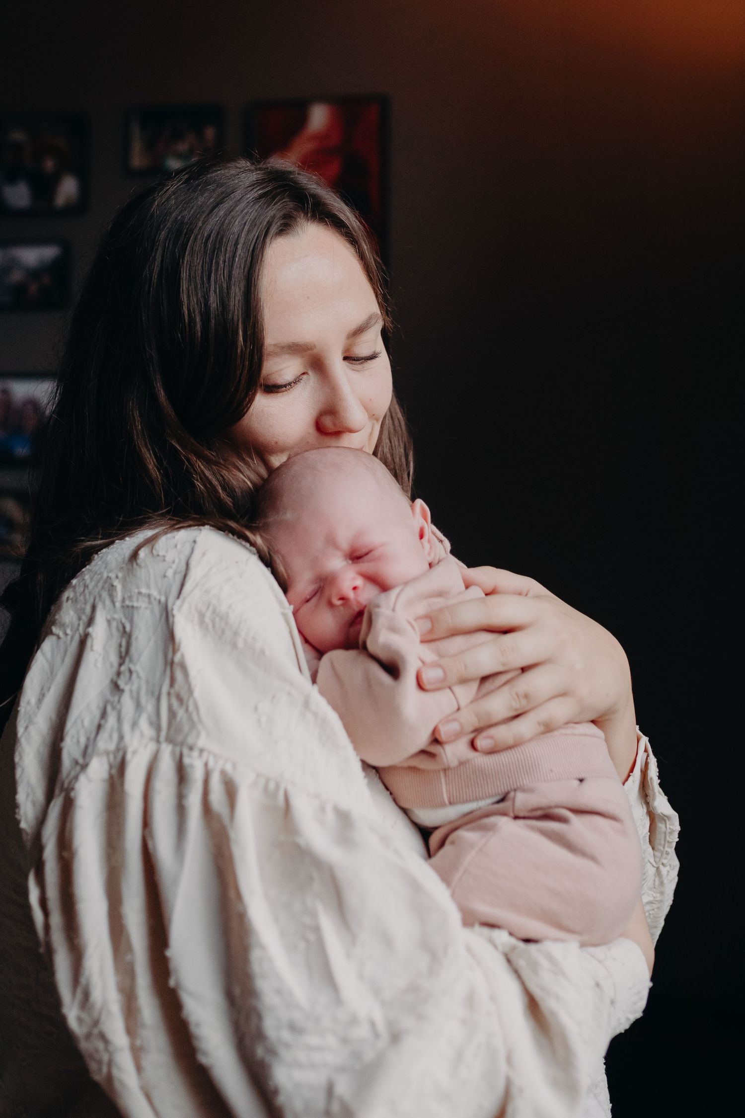 A parent in a white sweater lovingly kisses and holds their newborn baby in a series of intimate portraits.