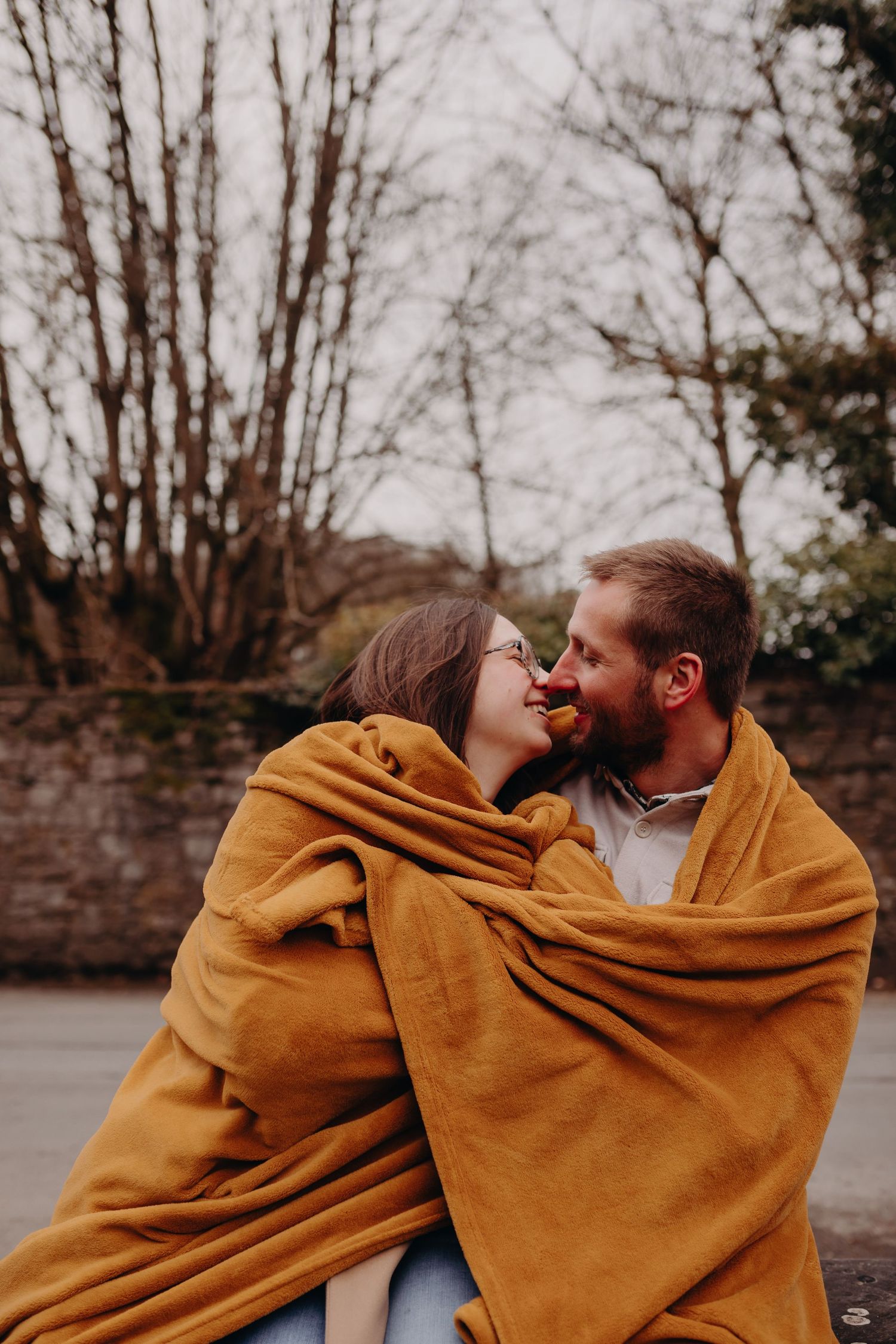 A romantic couple wrapped in a cozy mustard yellow blanket share an intimate moment outdoors on a winter day.