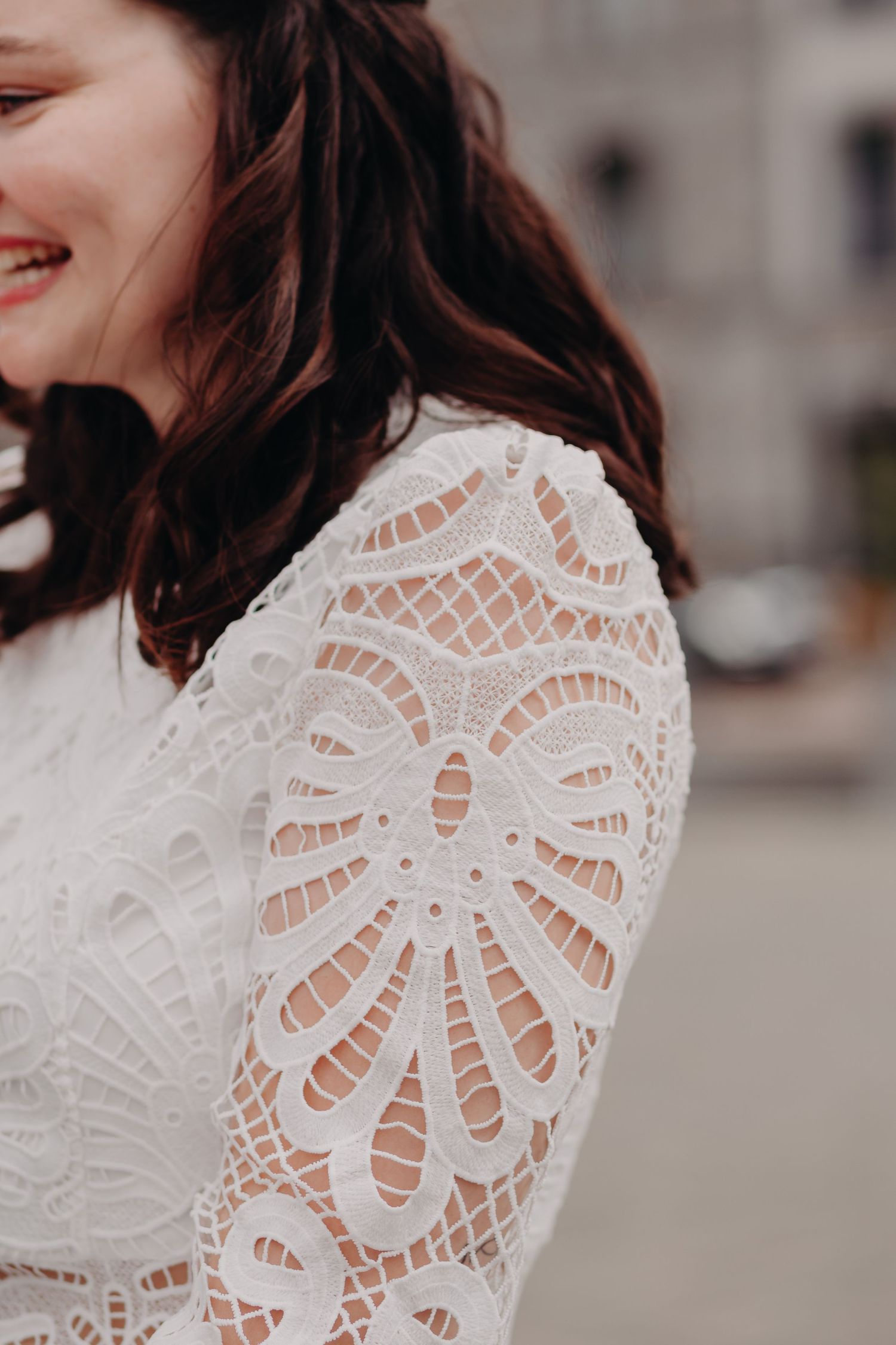 Close-up of delicate white lace wedding dress sleeve with intricate floral pattern detail.