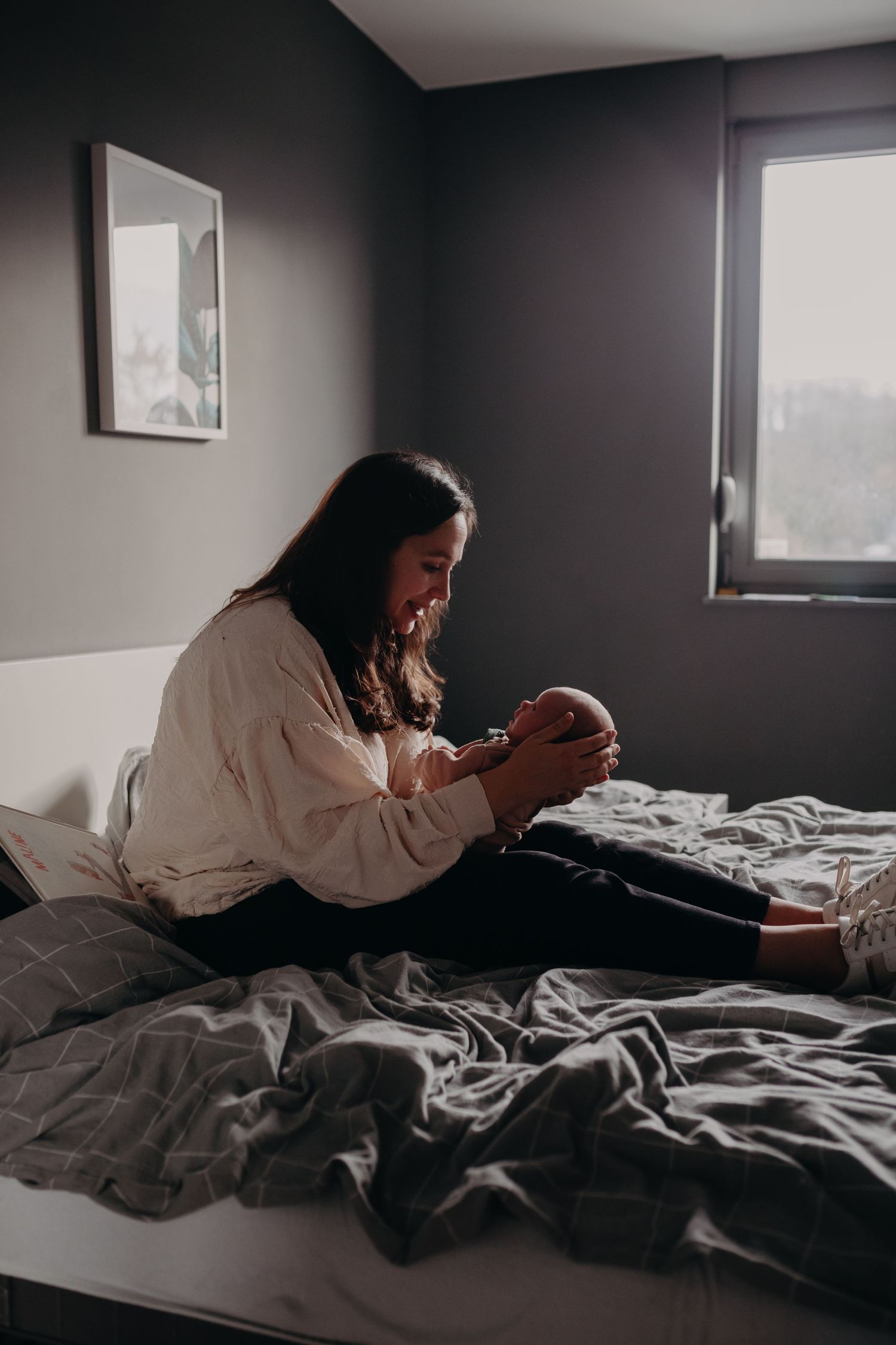 Person relaxing on unmade bed with grey bedding in moody bedroom lighting.