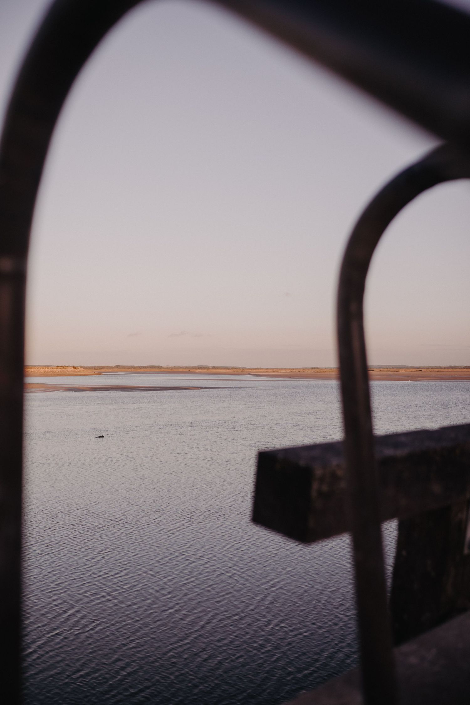 Scenic waterfront view framed through a window or opening at sunset, showing calm waters and distant shoreline.