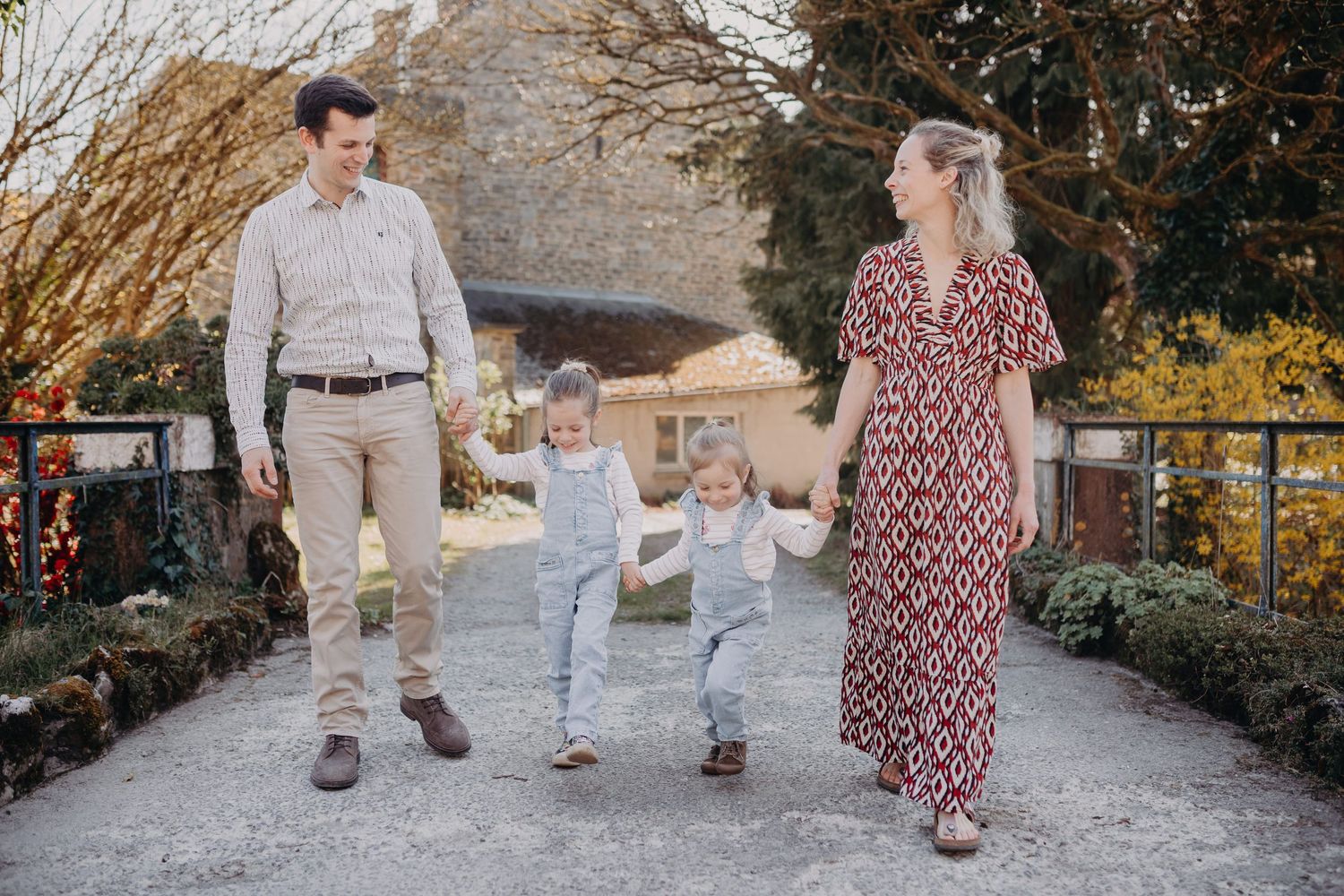 A family walks hand in hand along a garden path with two children between the parents on a sunny day.