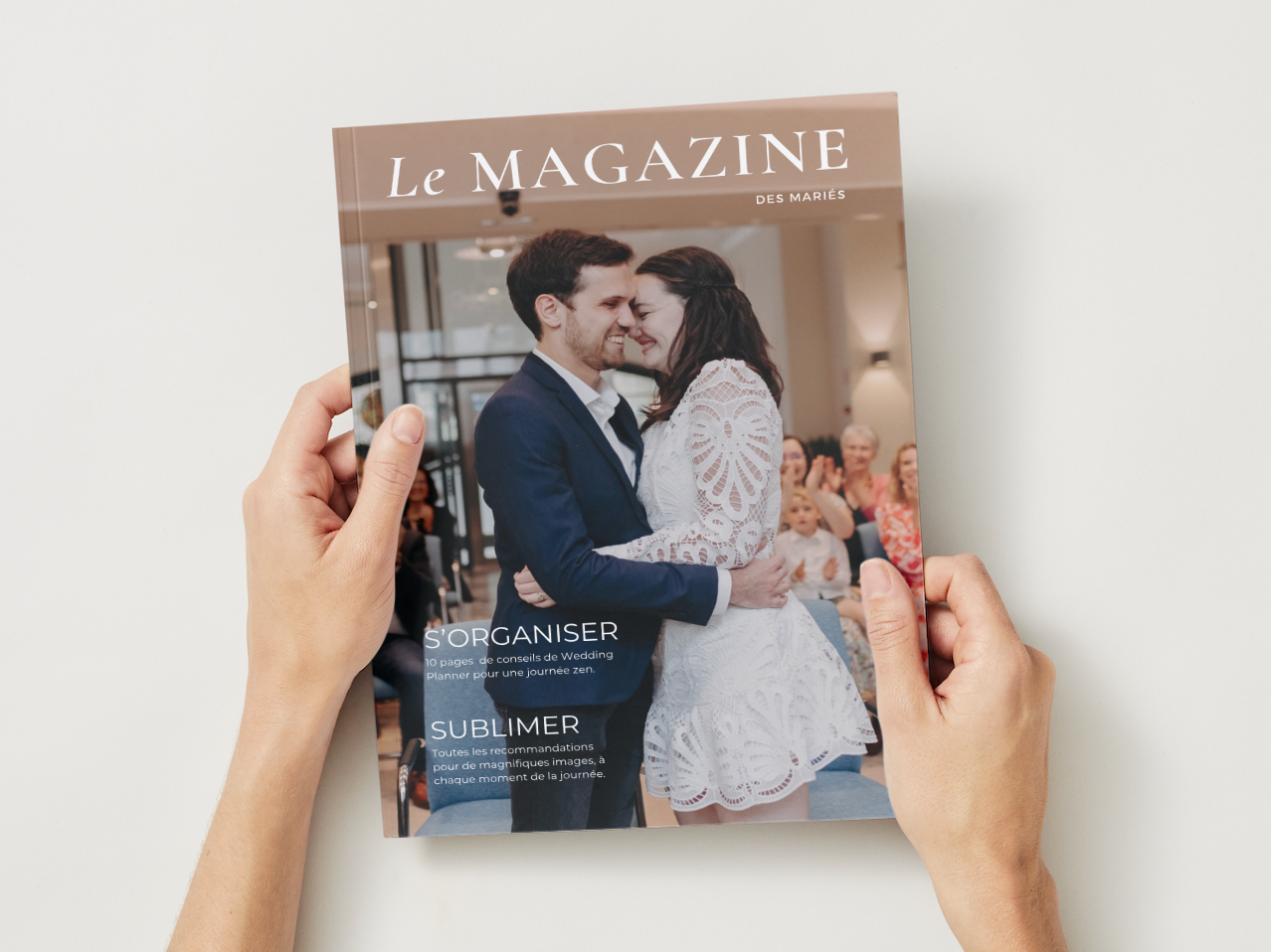Hands holding open a wedding magazine titled 'Le MAGAZINE' featuring a romantic couple in formal attire on the cover.