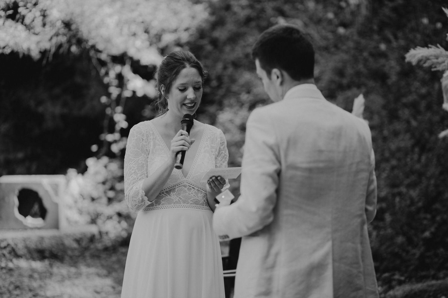 Black and white photo of an outdoor wedding ceremony with couple sharing personal vows in a garden setting.