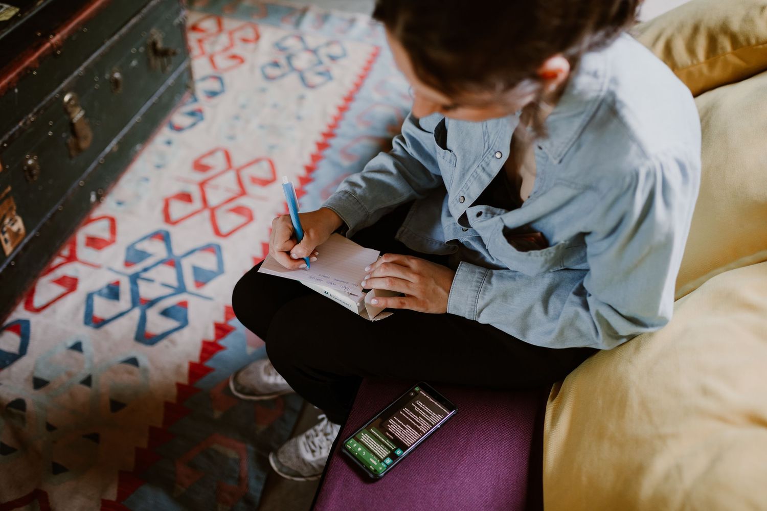 Small child seated on colorful patterned rug doing schoolwork in a light blue button-down shirt.