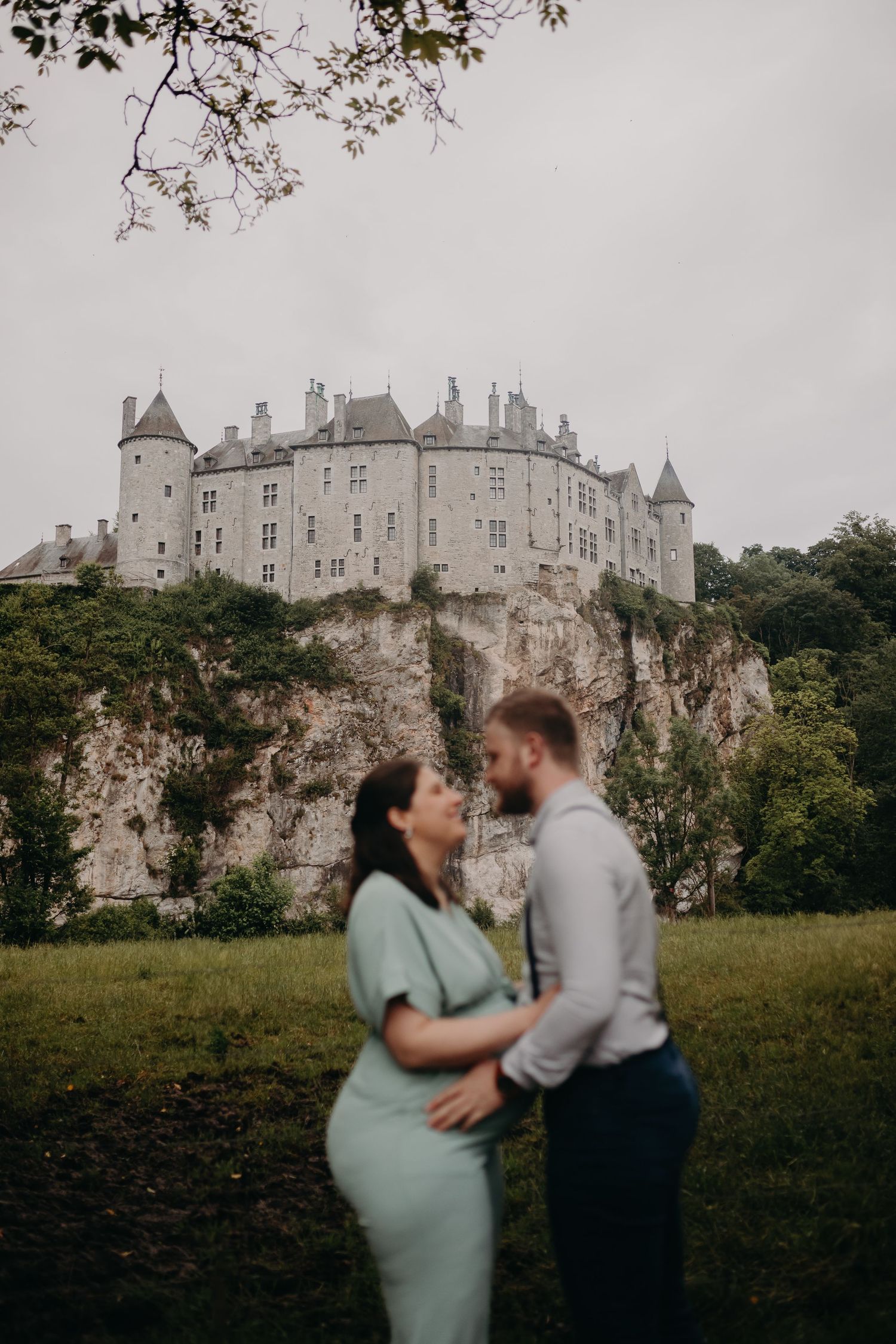 A romantic couple embraces in front of a majestic French chateau perched dramatically on limestone cliffs at dusk.