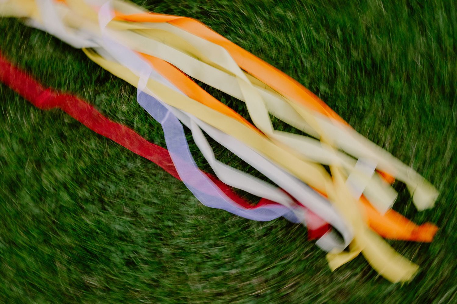 Colorful twisted ribbons of red, orange, yellow, white, and blue laid on green grass.
