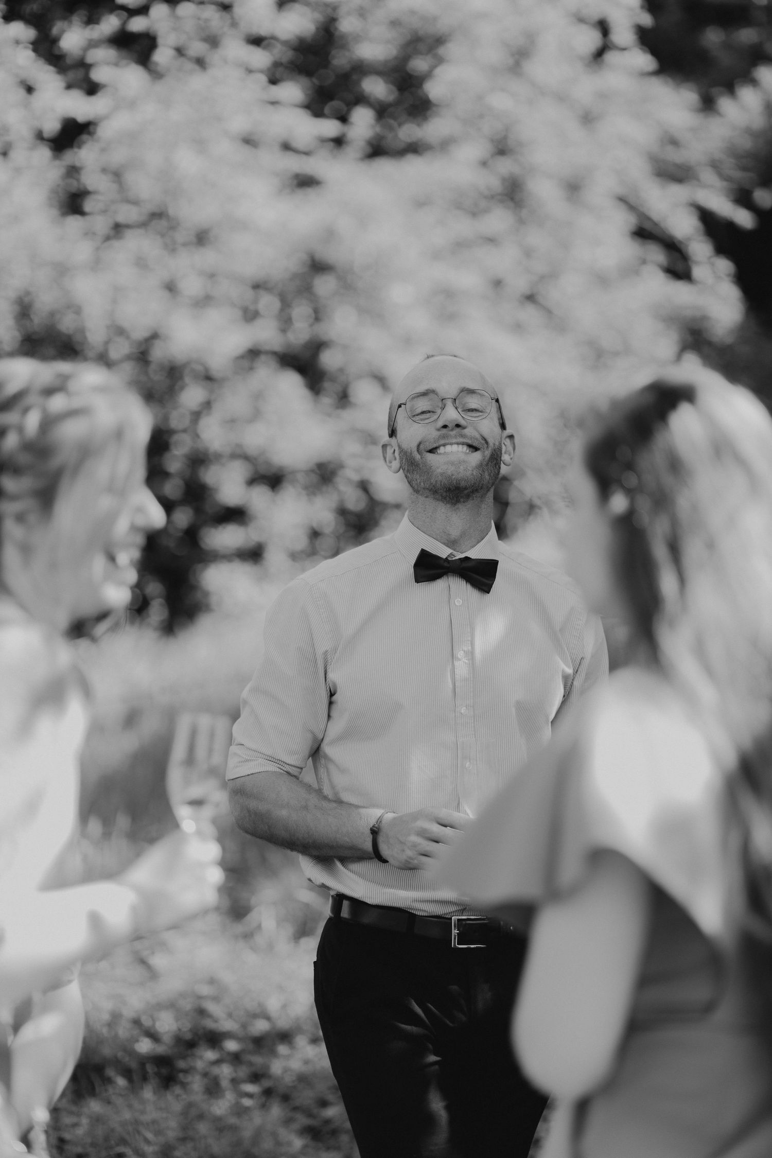 Black and white photo of someone wearing a bow tie and dress shirt laughing joyfully at an outdoor event.