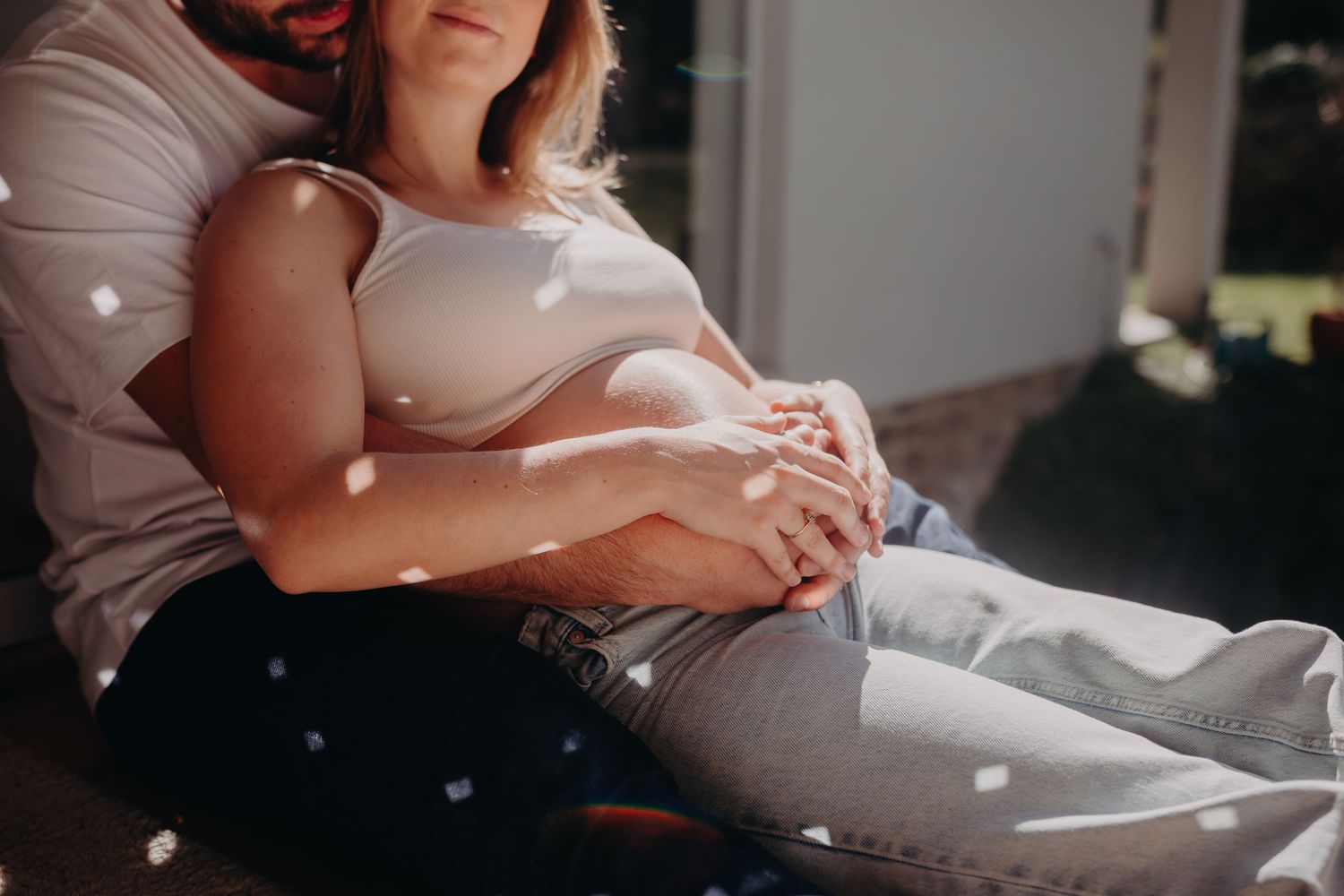 Sunlit maternity photo shows pregnant woman in casual attire resting peacefully on porch in natural lighting.