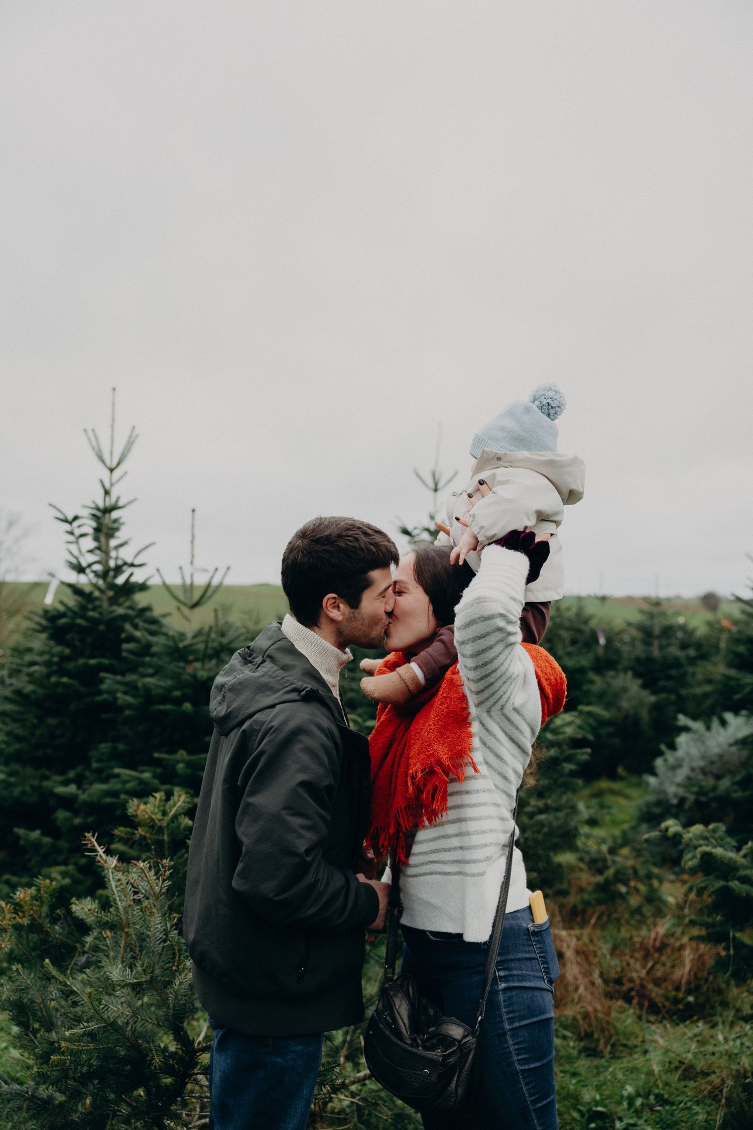 A couple shares tender moments while hiking through an evergreen forest on a cloudy day.
