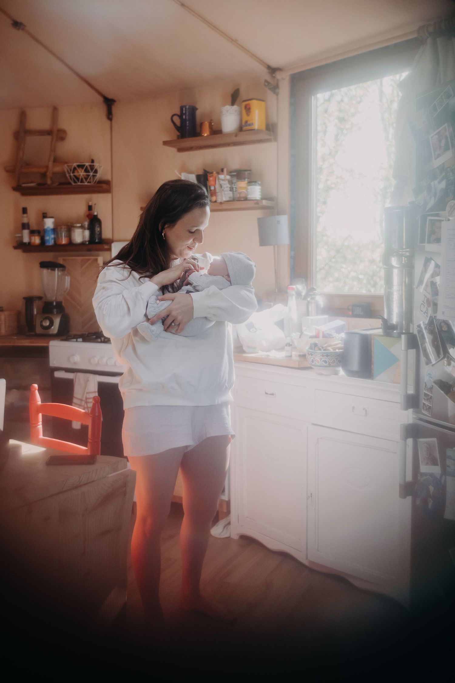 A person in a white shirt works in a sunlit kitchen space with wooden shelves and countertops.