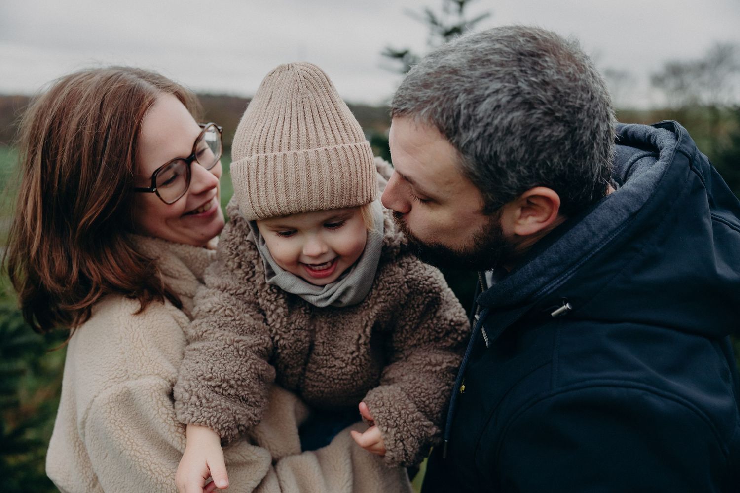 A family embraces outdoors in winter wearing cozy sweaters and knit accessories.