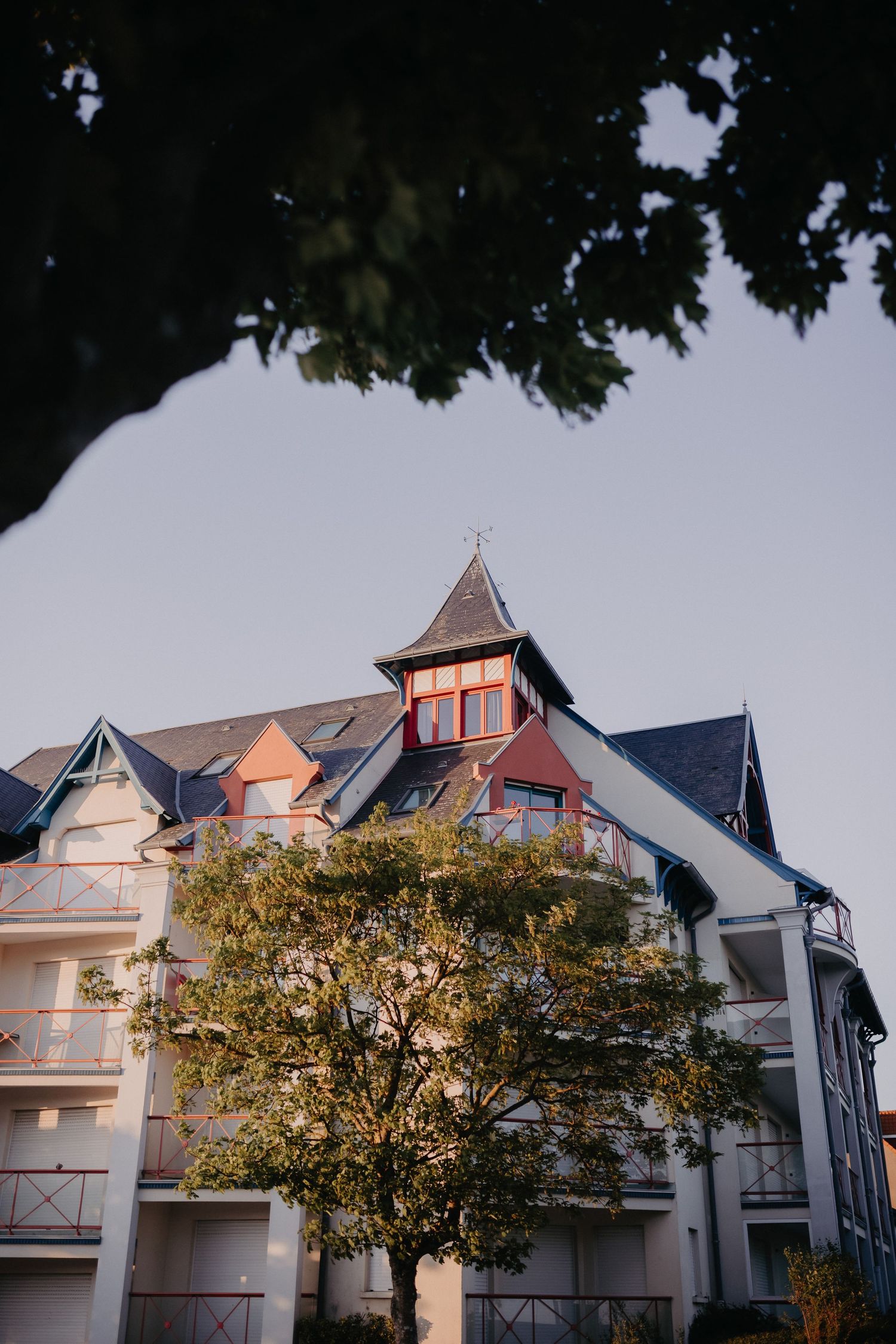 Elegant European-style apartment building with a distinctive tower and balconies framed by autumn trees at dusk.