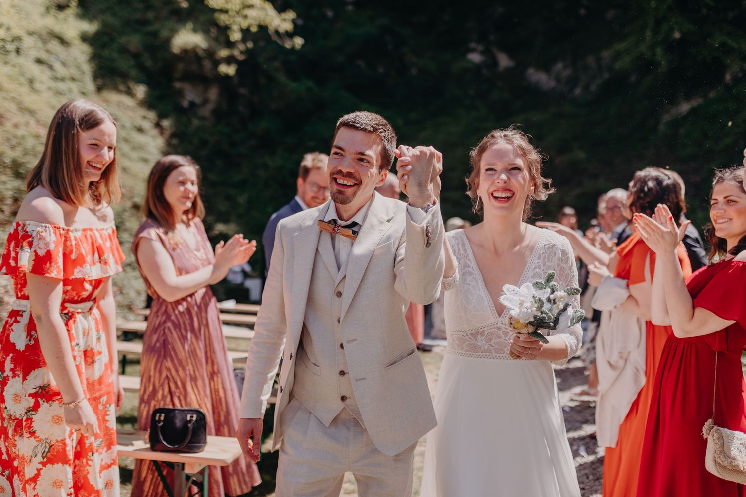 A joyful wedding celebration outdoors with guests wearing coral and red dresses celebrating the happy couple.