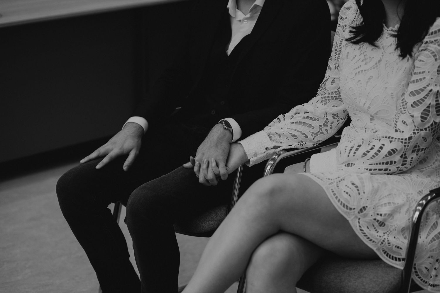 Black and white intimate photo showing hands on a sofa during couple's romantic moment wearing formal attire.