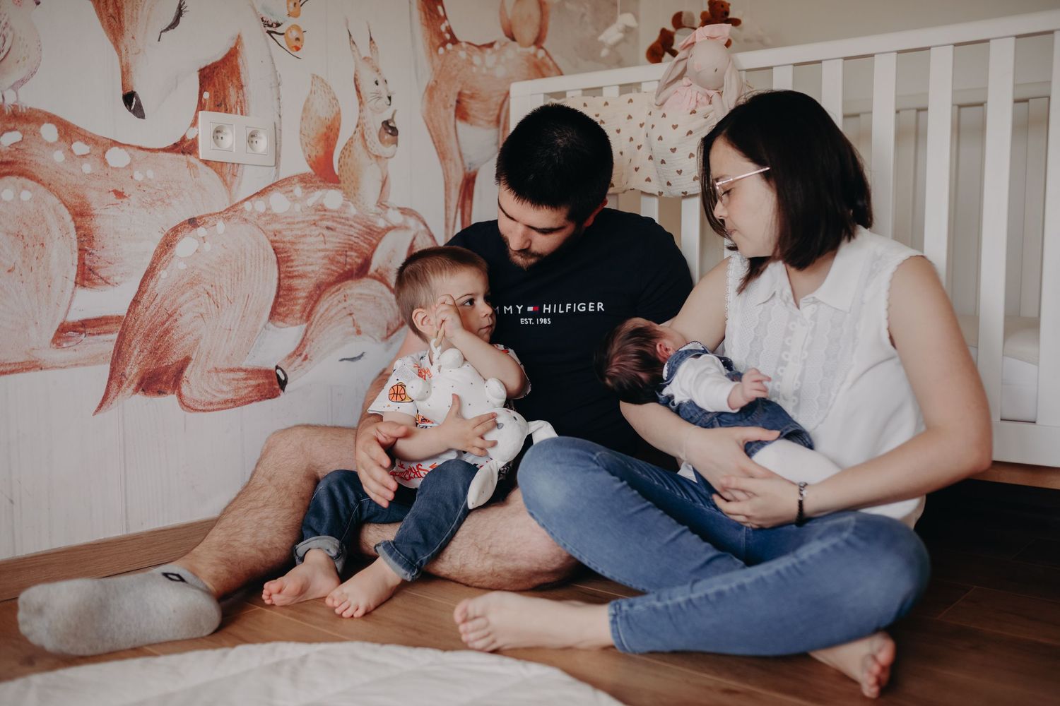 Family sitting on floor in front of wall with pink mural while feeding and holding young babies.