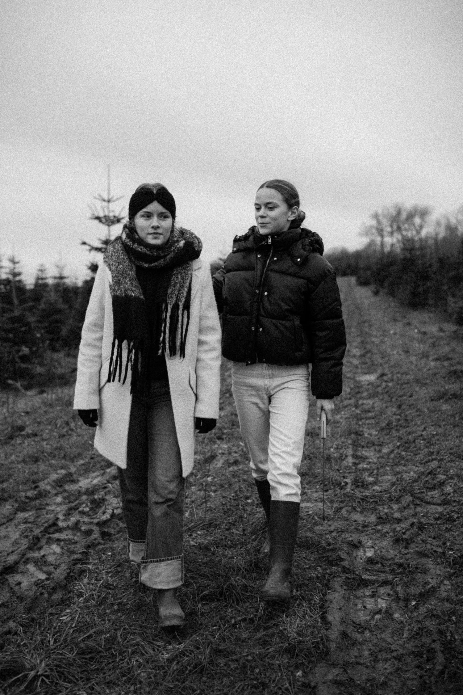 Black and white sequence of two people walking together across a barren field in winter clothing and scarves.
