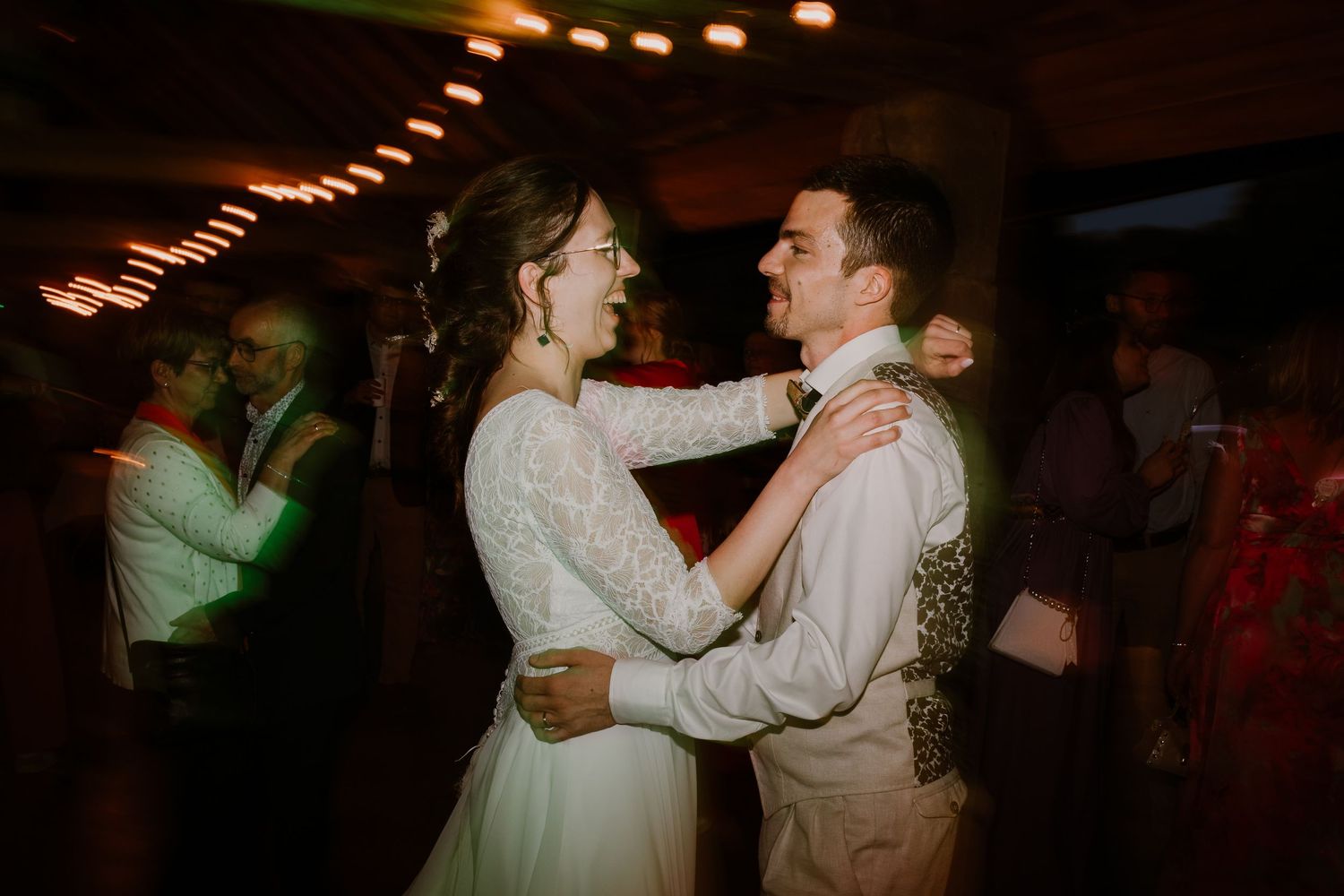 A couple shares their romantic first dance at a dimly lit wedding reception with twinkling lights overhead.