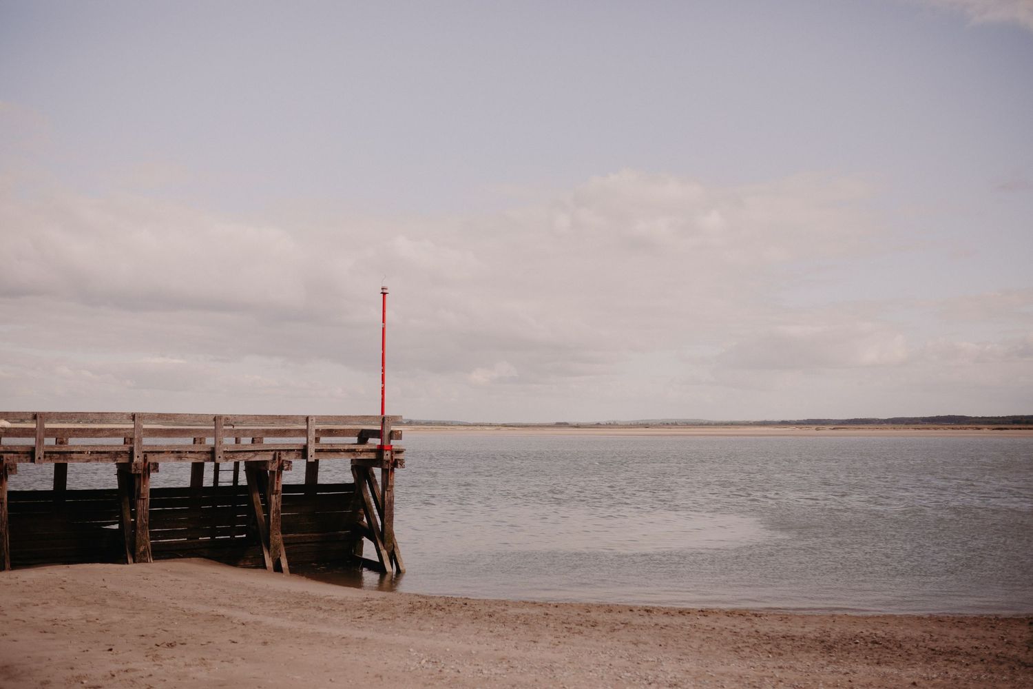 A wooden fishing pier extends into calm waters under an overcast sky at dusk.