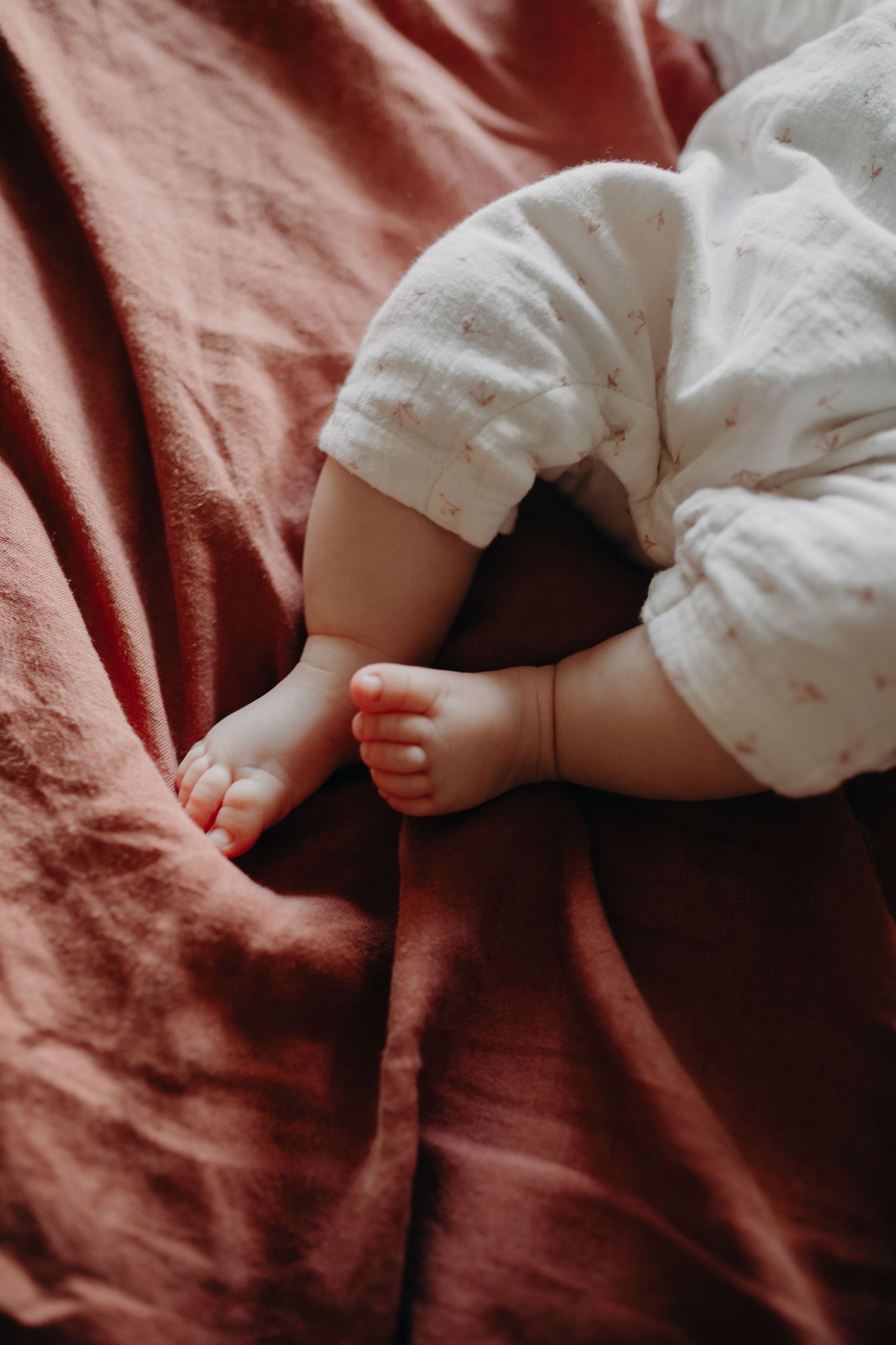 Small baby's feet resting on soft burgundy bedding in a gentle sleeping pose.