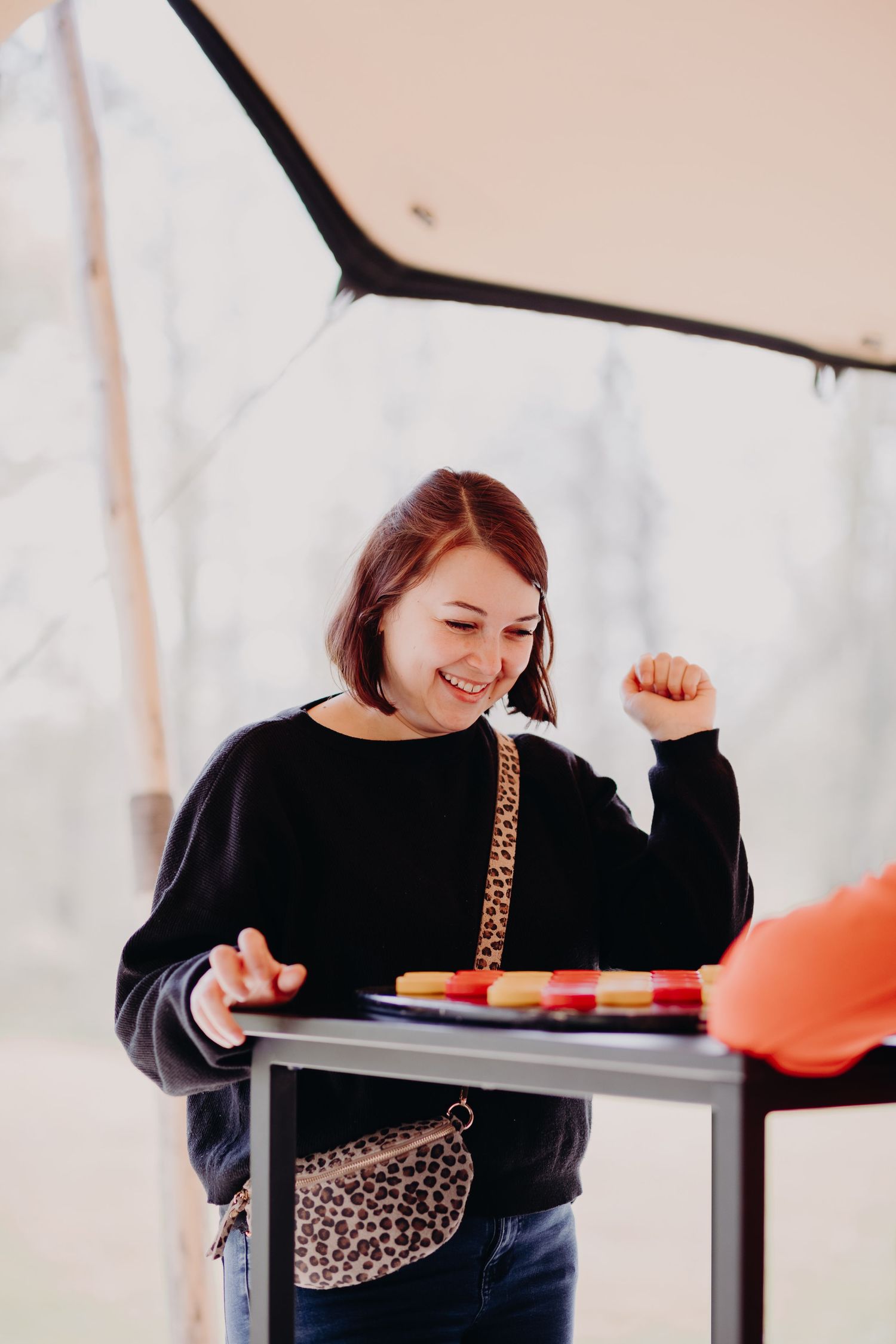 Person in black sweater with leopard print bag smiles while standing at counter with colorful items.