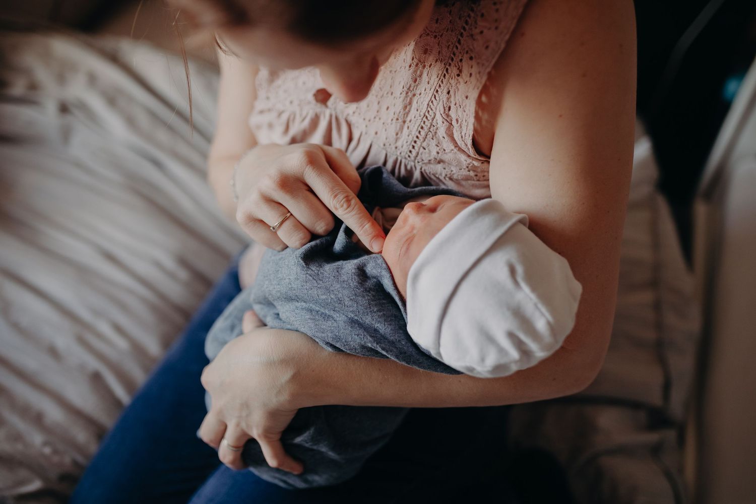Mother cradles sleeping infant while resting on bed during intimate breastfeeding moment.