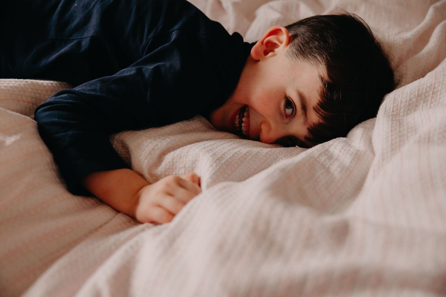 A person in a dark sweater lies on white bedding while resting their head on soft pillows.