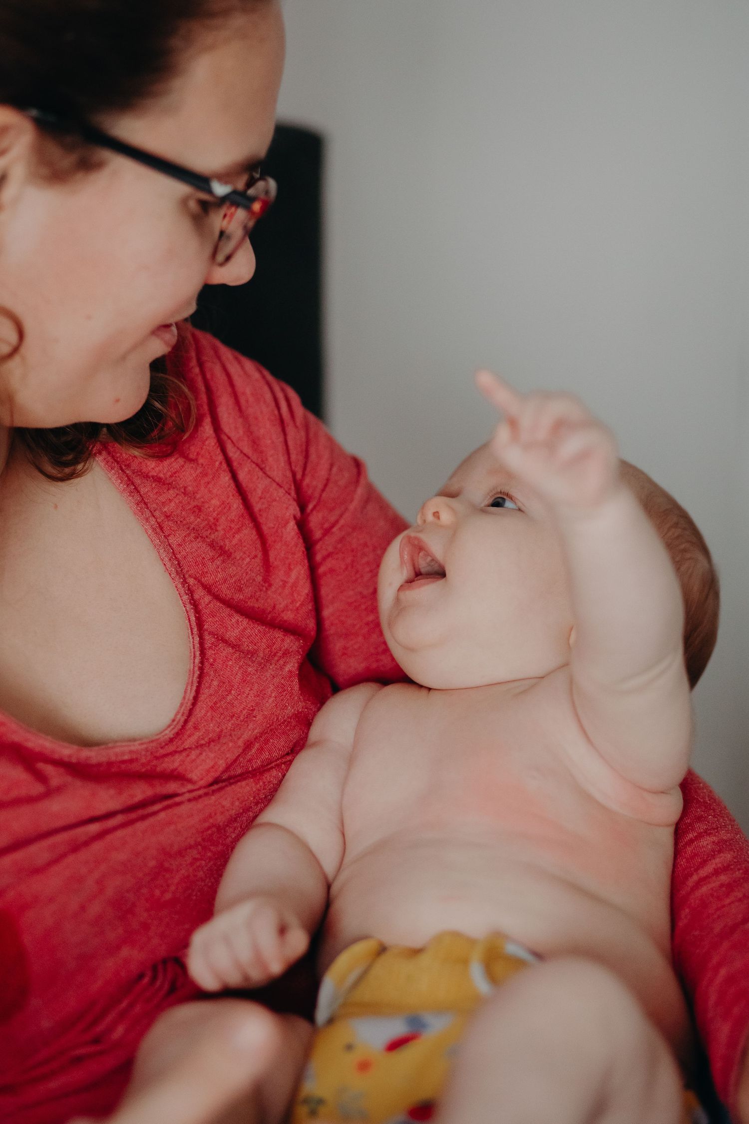 A parent in a red shirt shares a tender moment with their baby wearing yellow pants.