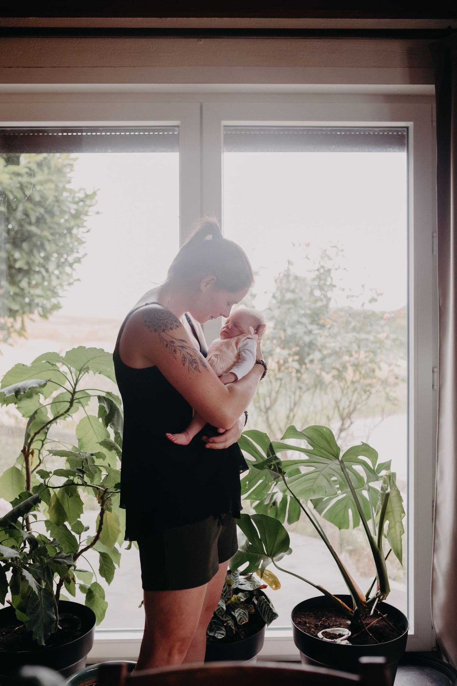 A person wearing black clothing tends to houseplants arranged on a windowsill in natural light.