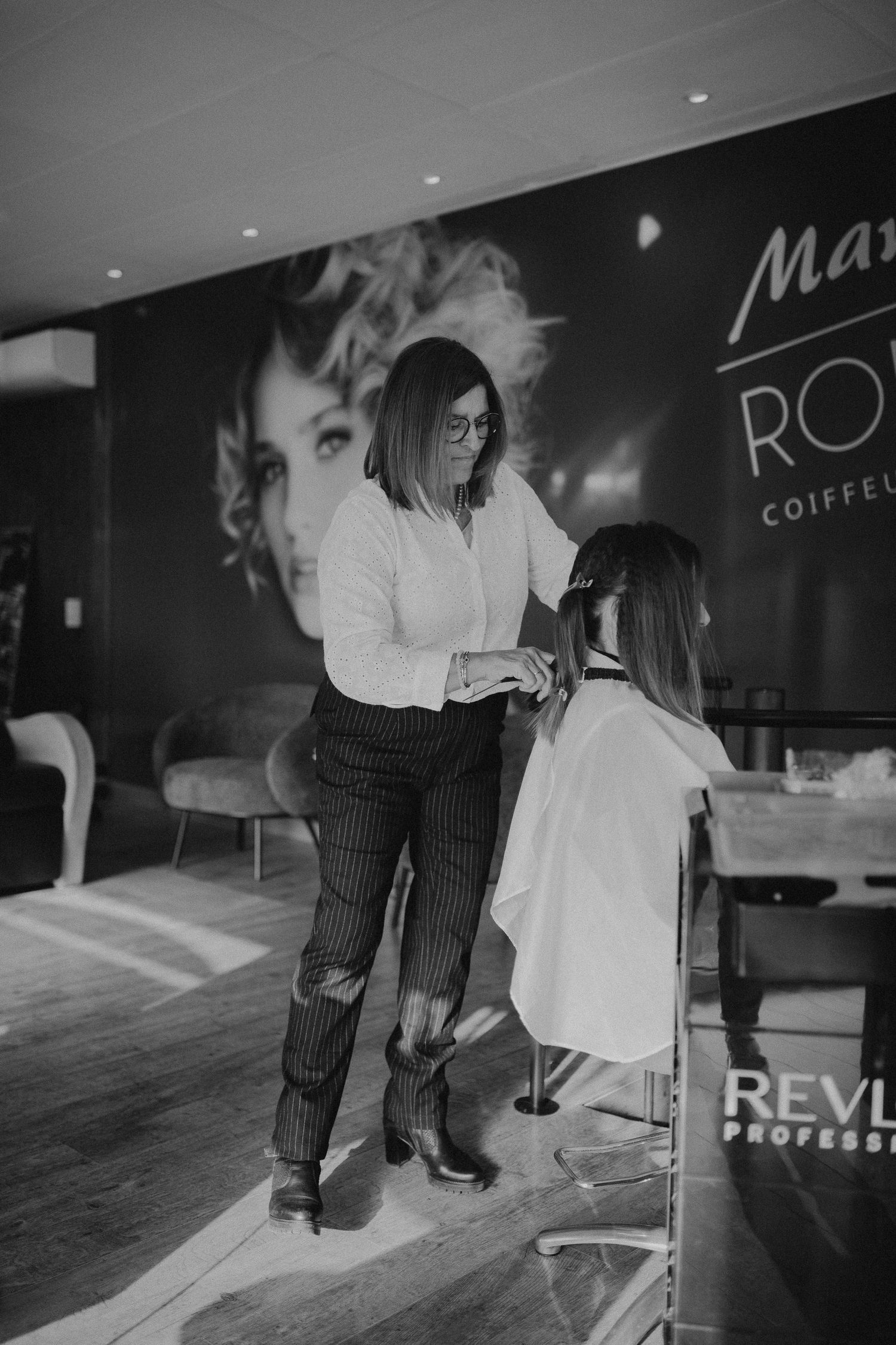 A stylist works on a client's hair in a modern salon with a large decorative wall mural.
