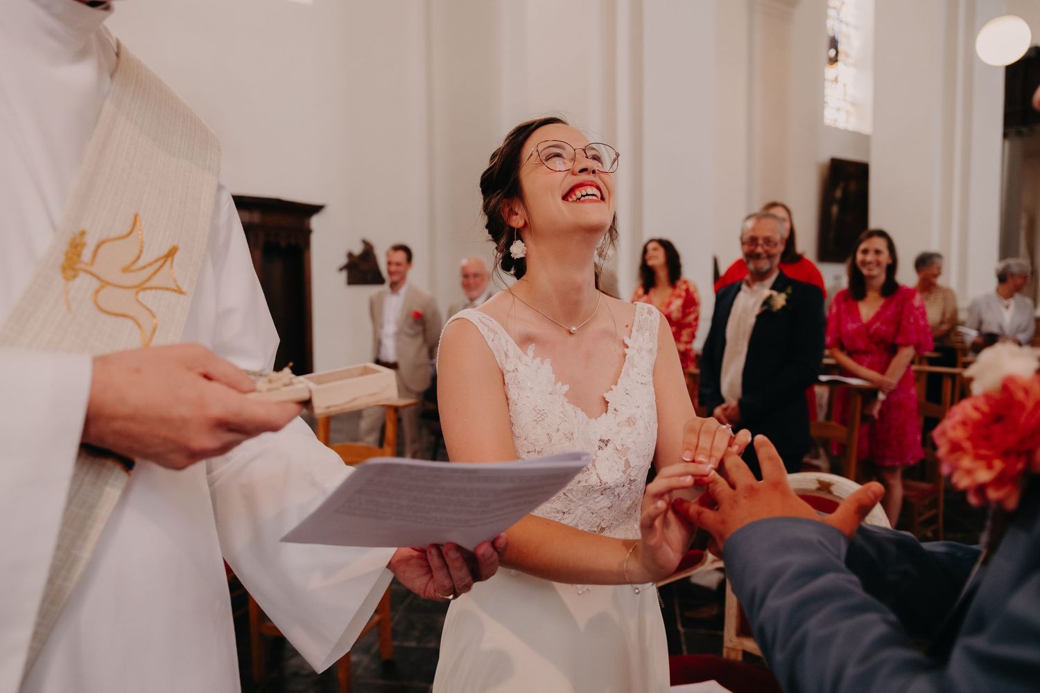A group of wedding guests react with laughter and joy during a celebration in an elegant white venue.