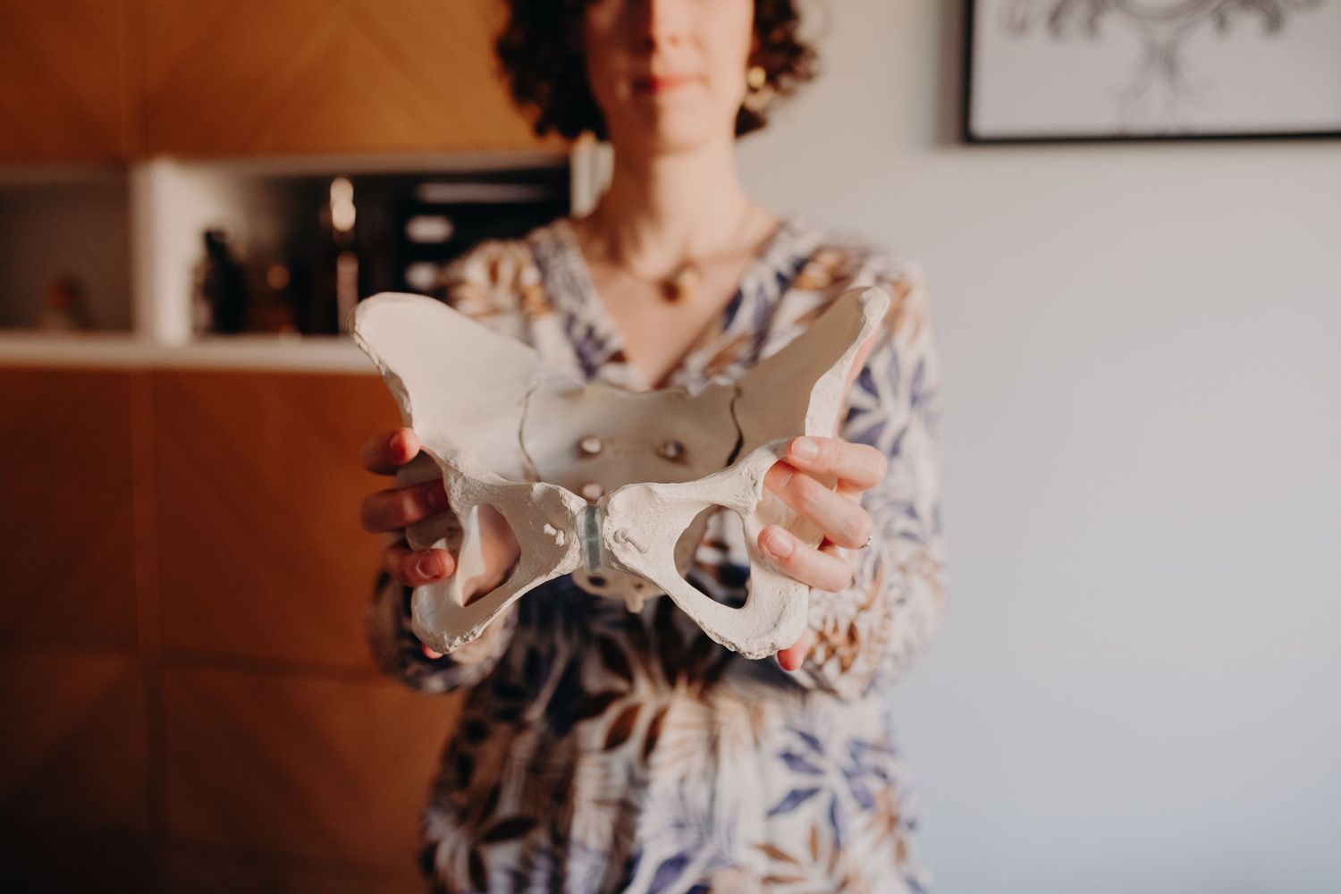 A person wearing a floral dress holds a vintage ceramic teacup in front of a light-colored wall.