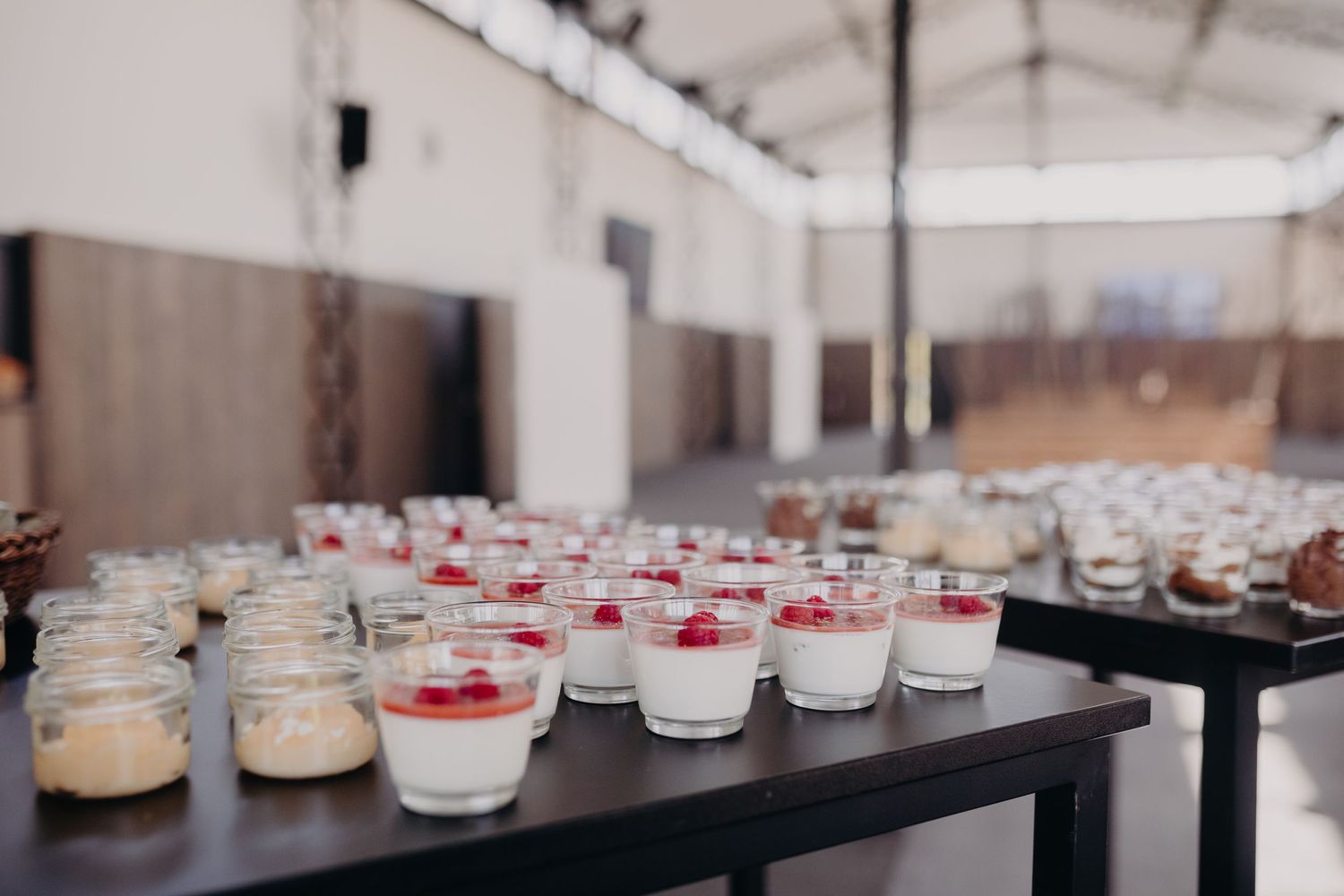 Individual dessert cups with layered cream and red toppings arranged on dark tables at an event venue.