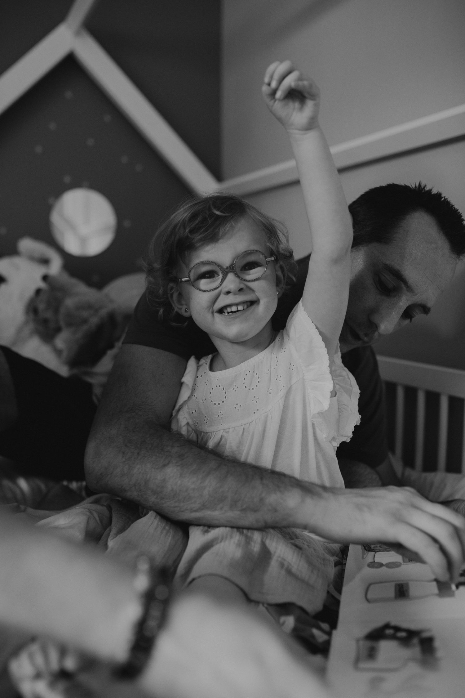 A delighted child wearing glasses raises their arm in celebration while being supported by a grown-up in a heartwarming moment.