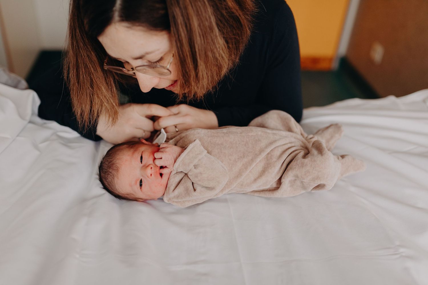 A tender moment captured as a parent leans over their newborn baby lying on white bedding.