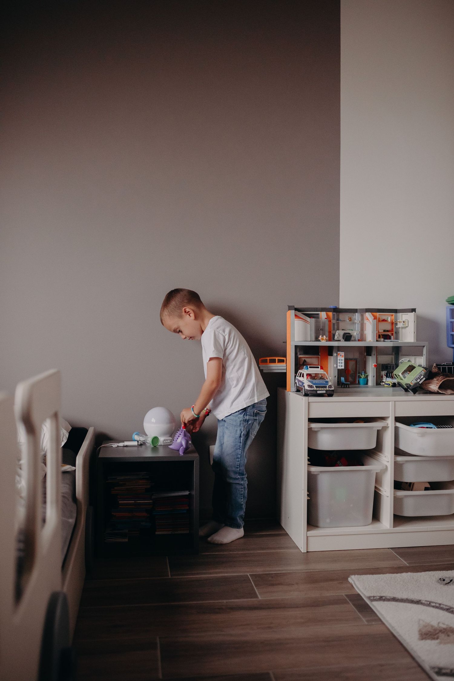 A person wearing a white t-shirt and jeans organizes a storage unit in a minimalist room with wood flooring.