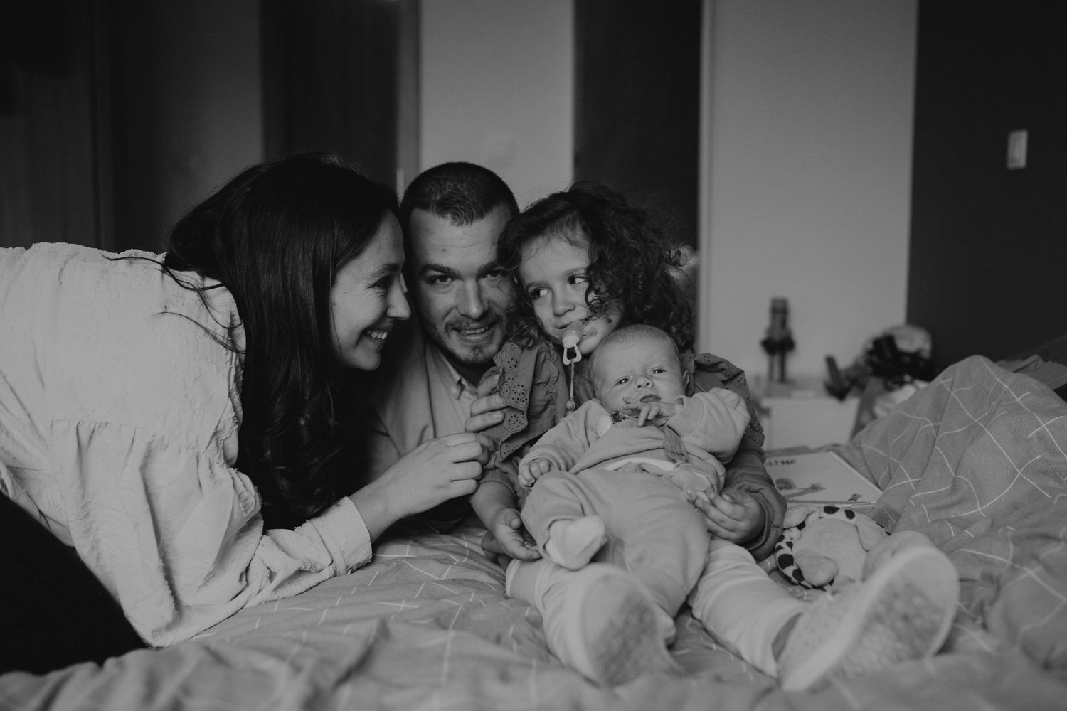 A series of black and white photos showing tender family moments of parents and children sleeping together.
