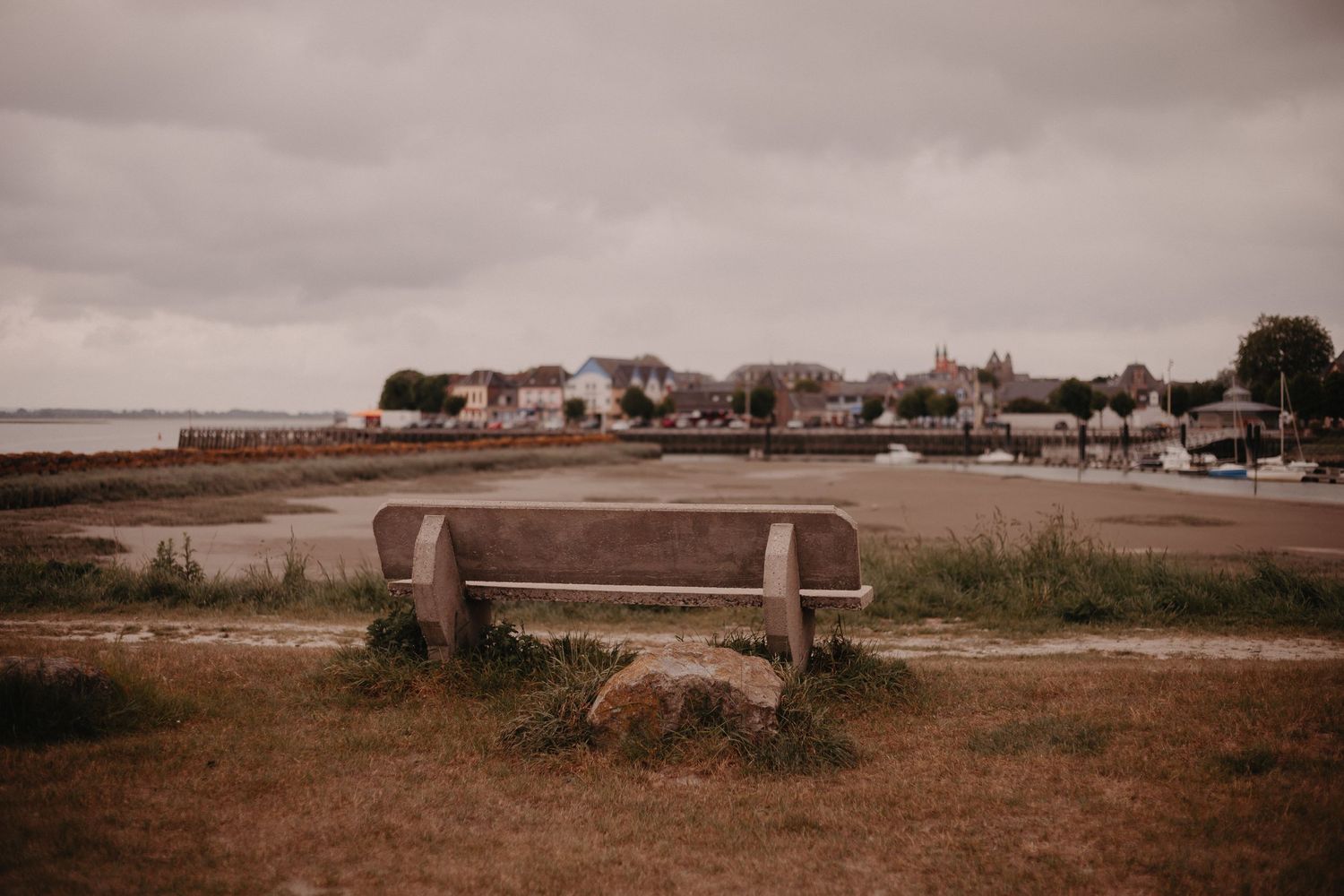 Empty wooden bench overlooking coastal homes and harbor on overcast day in seaside town.