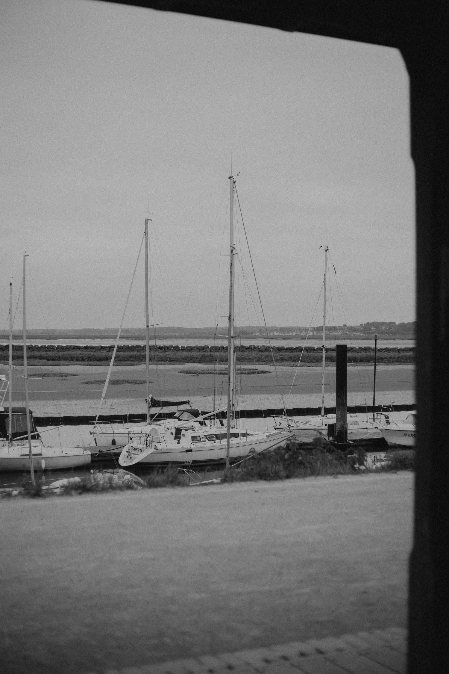 Black and white photograph of sailboats moored at a quiet marina during low tide.