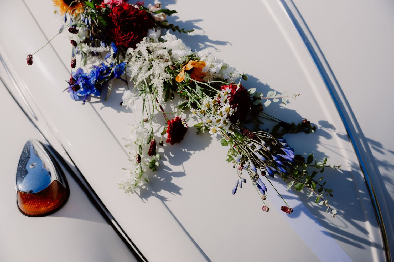 Colorful wildflower bouquet with red, blue, and white blooms resting on white surface.