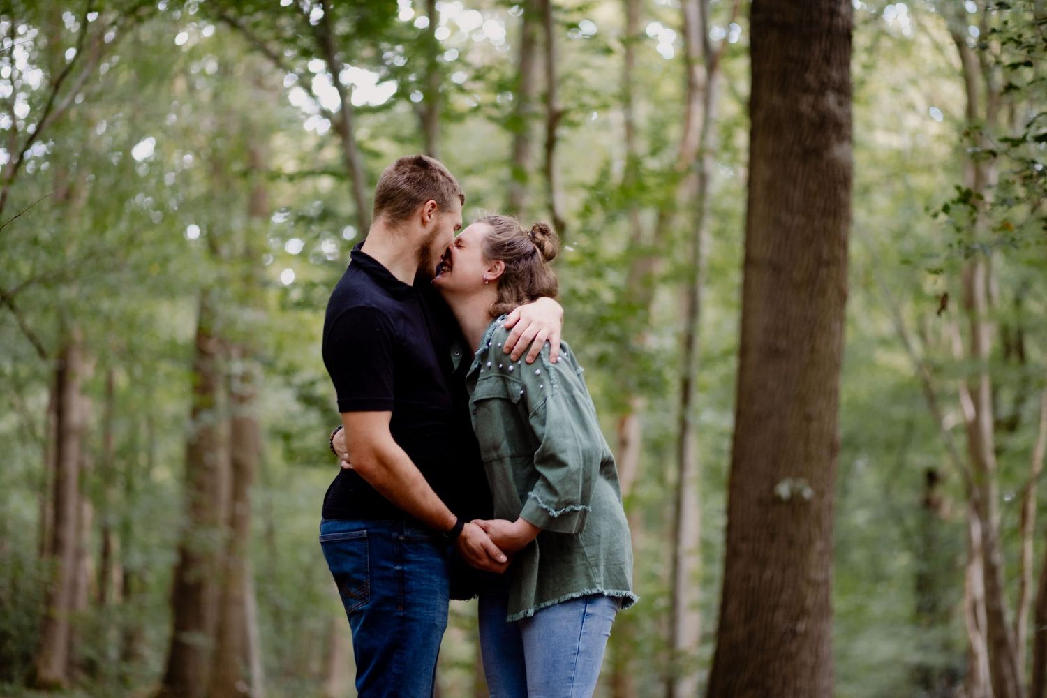 A romantic couple shares a tender moment together while standing in a serene forest setting.